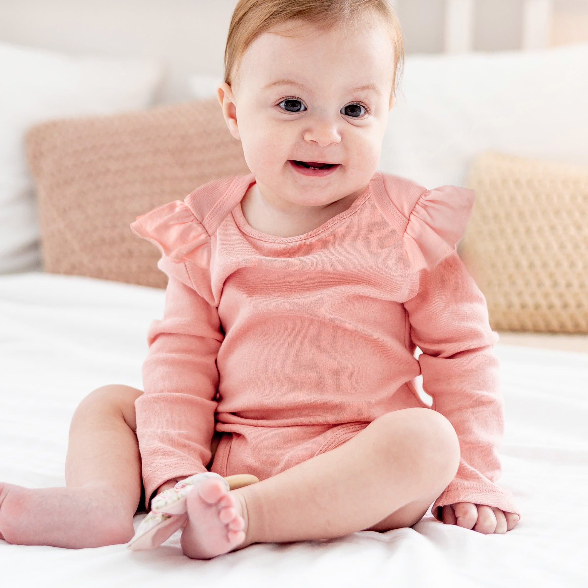Baby in a pink outfit sitting on a white surface with a blurred background