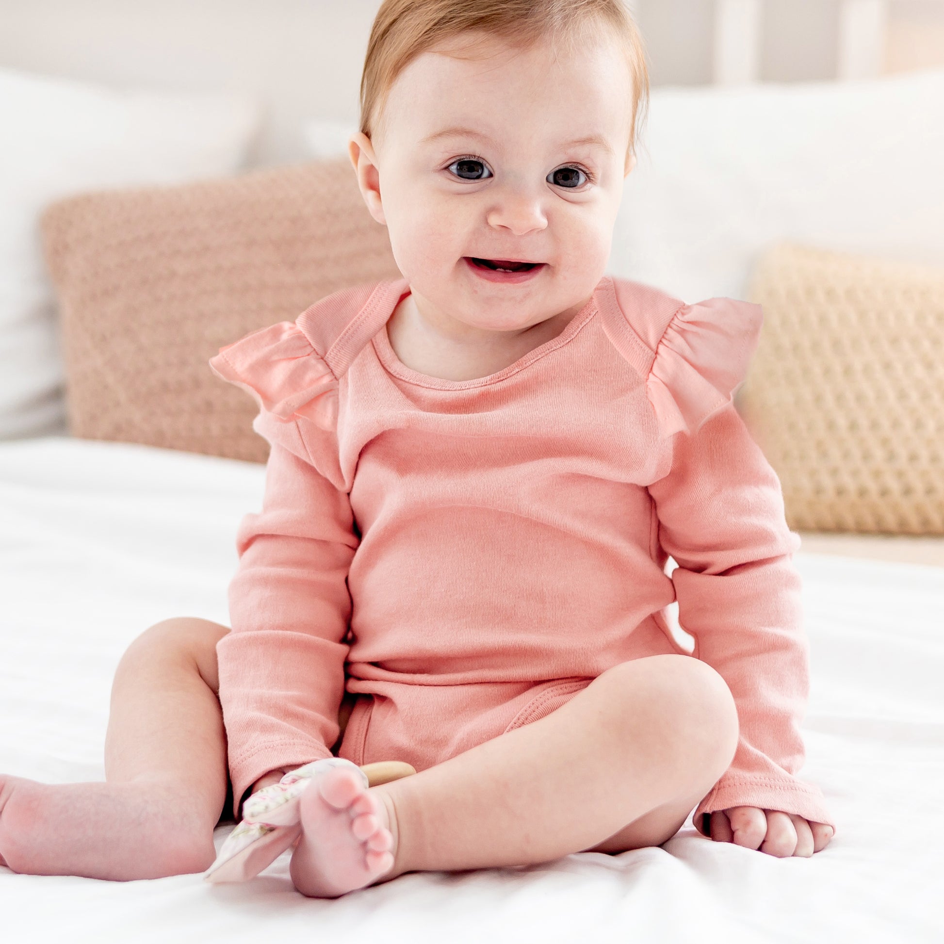 Baby in a pink outfit sitting on a white surface with a blurred background