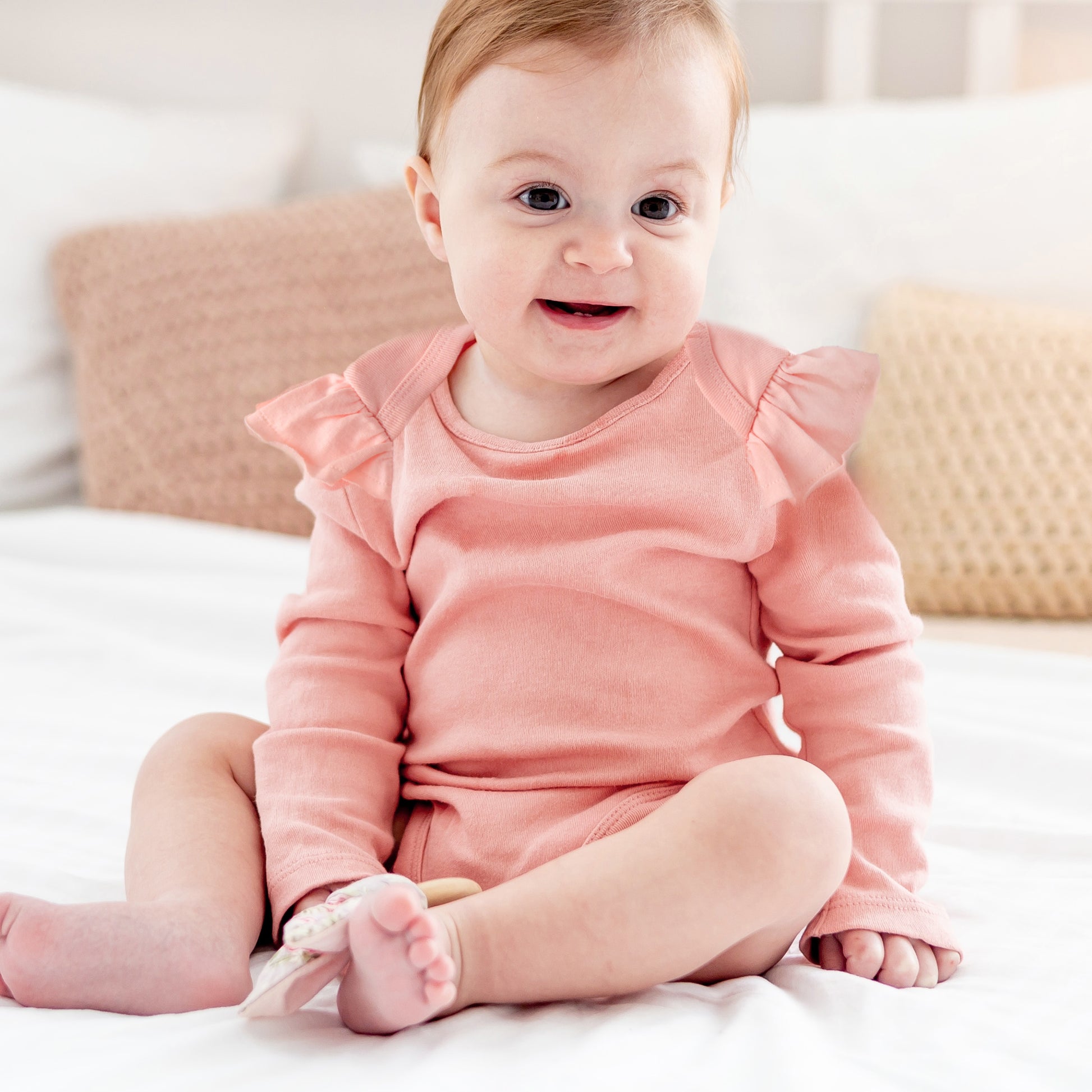 Baby wearing a pink outfit sitting on a bed.