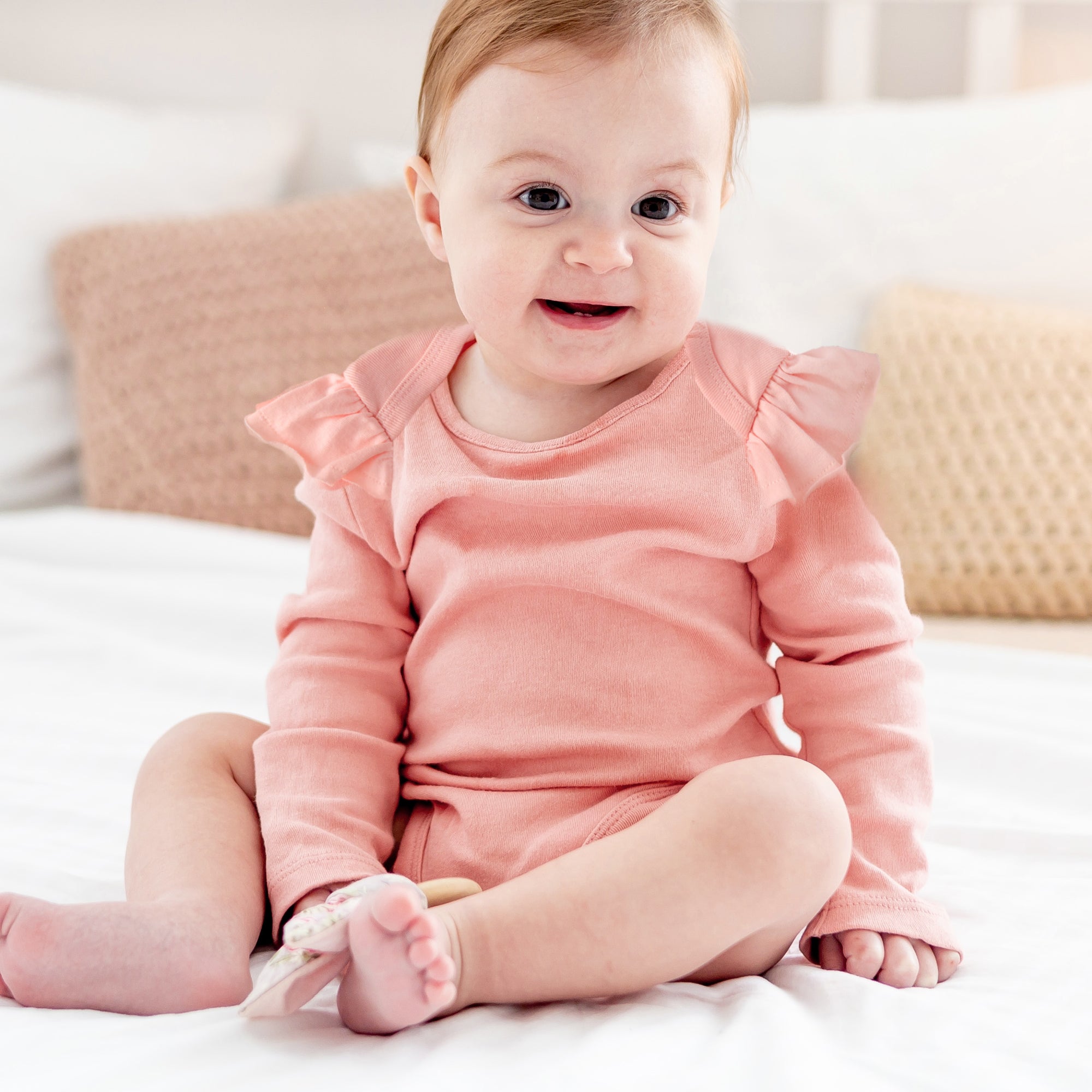Baby wearing a pink outfit sitting on a bed.