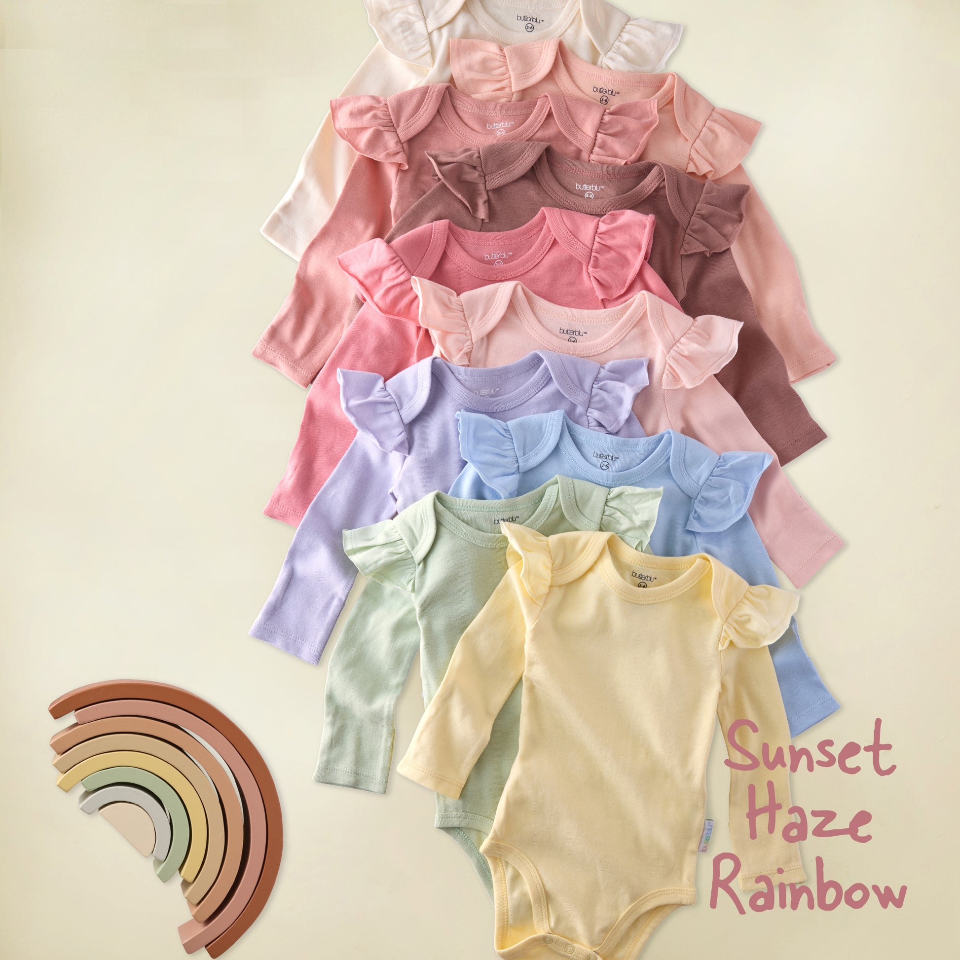 Stack of colorful baby bodysuits with a rainbow toy on a light background
