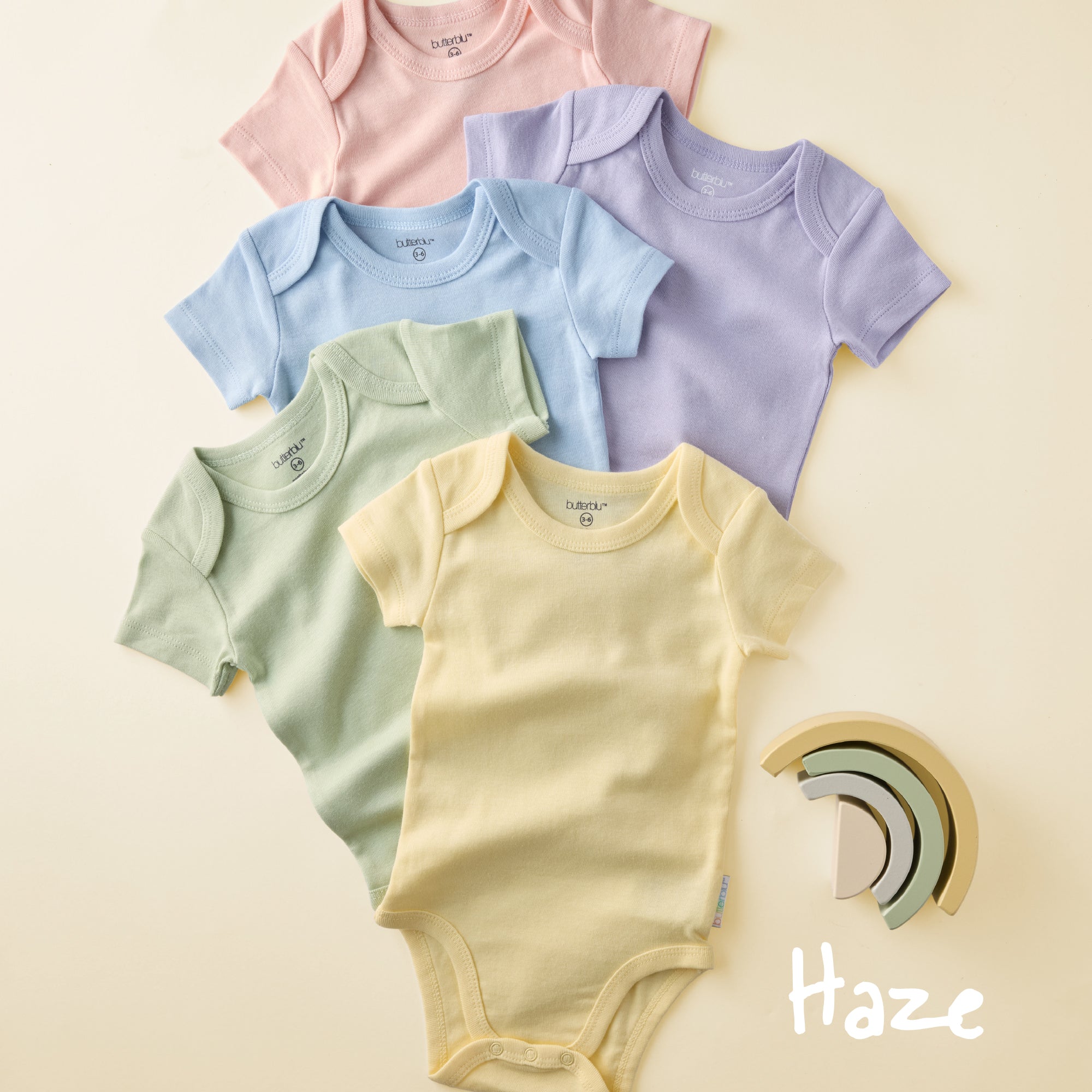 Five colorful baby bodysuits on a beige background with 'Haze' branding.