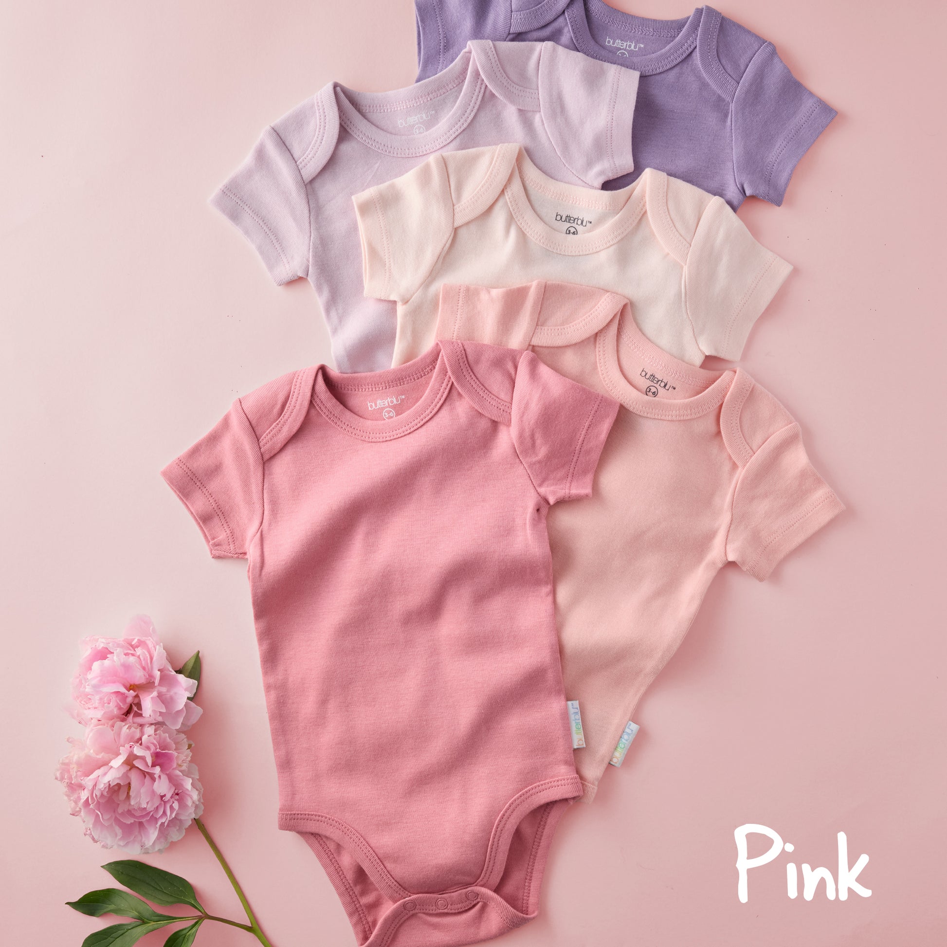 Collection of baby bodysuits in pink and purple on a light pink background with a flower.