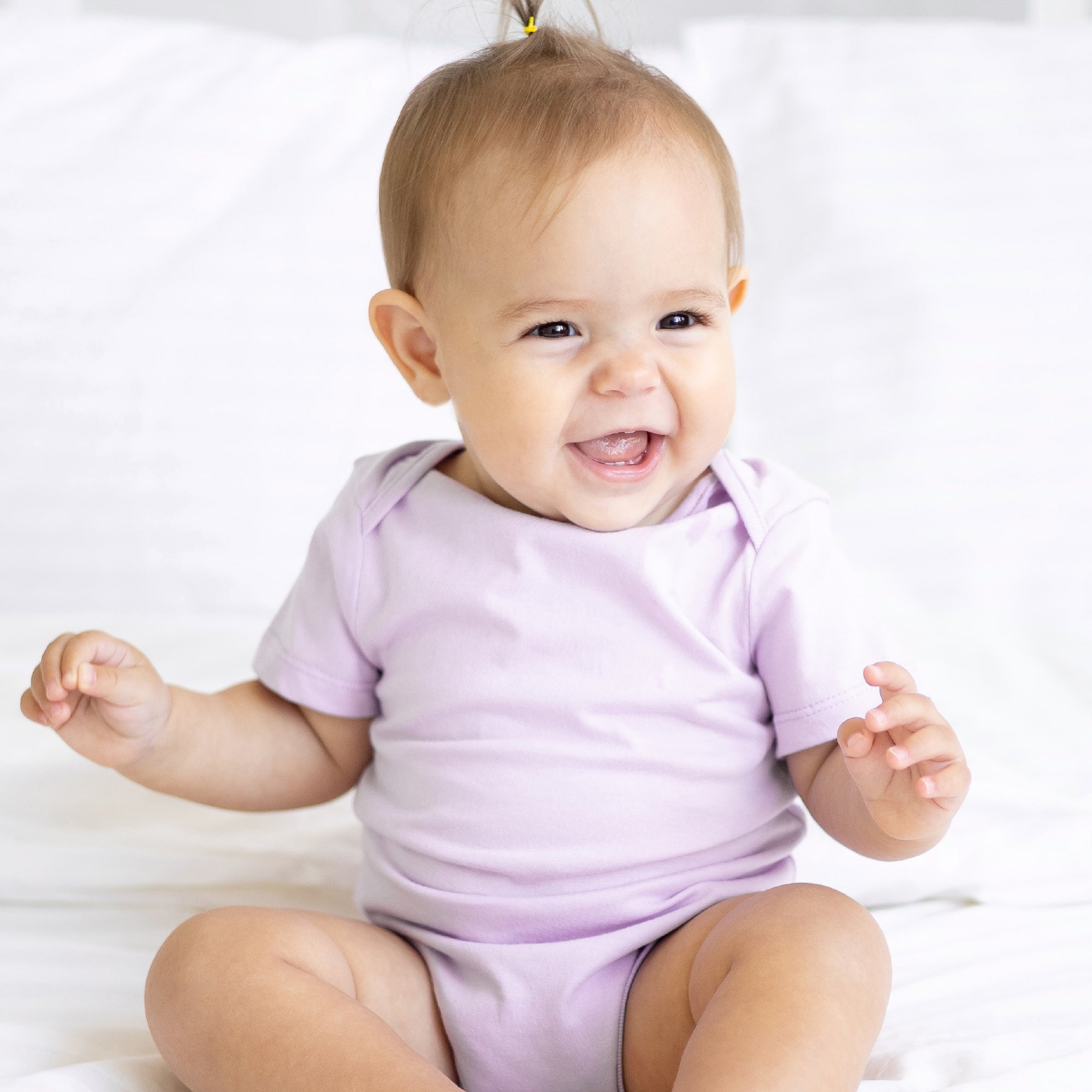 Baby wearing a purple onesie sitting on a white surface