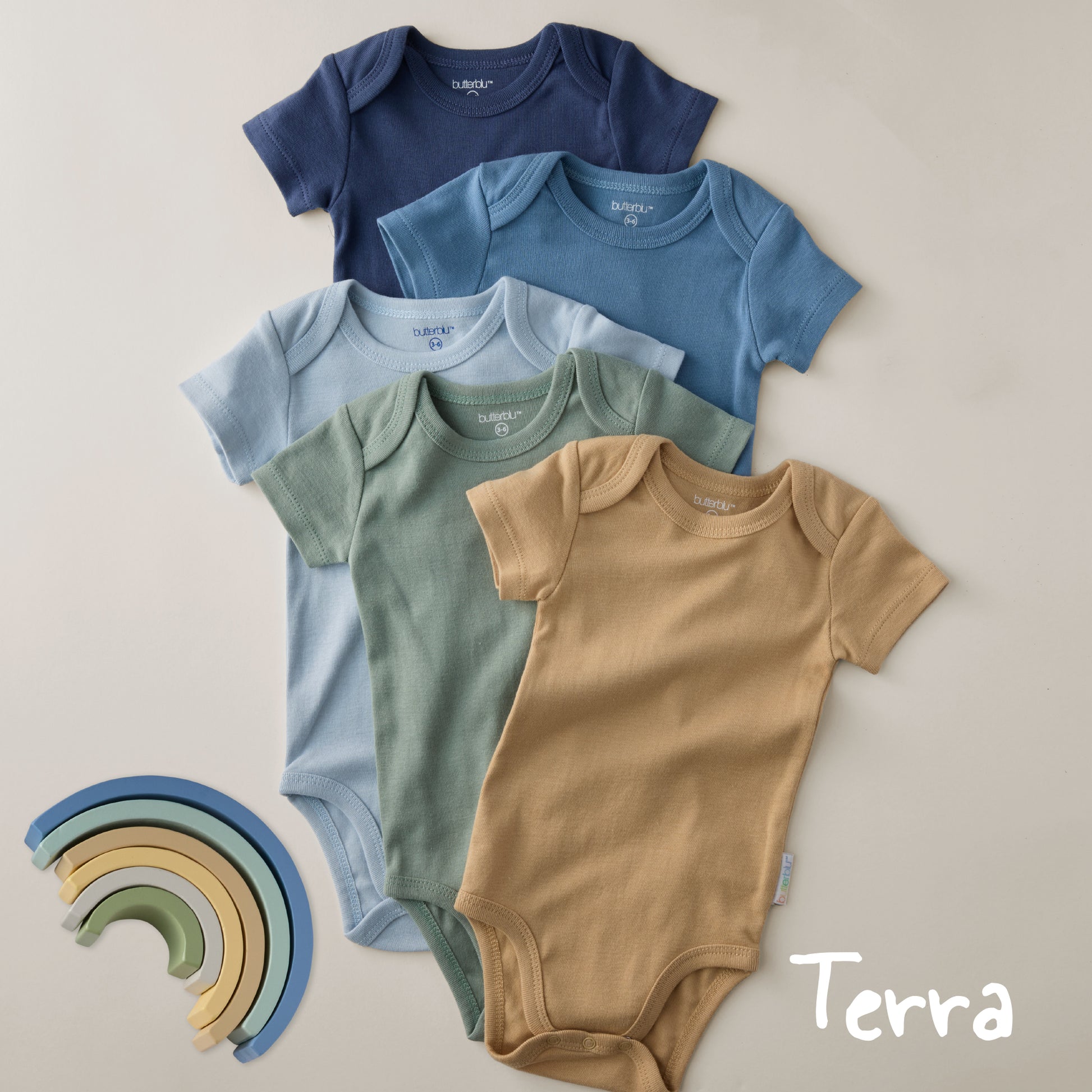 Five baby bodysuits in blue, green, and brown on a beige background with a rainbow toy.
