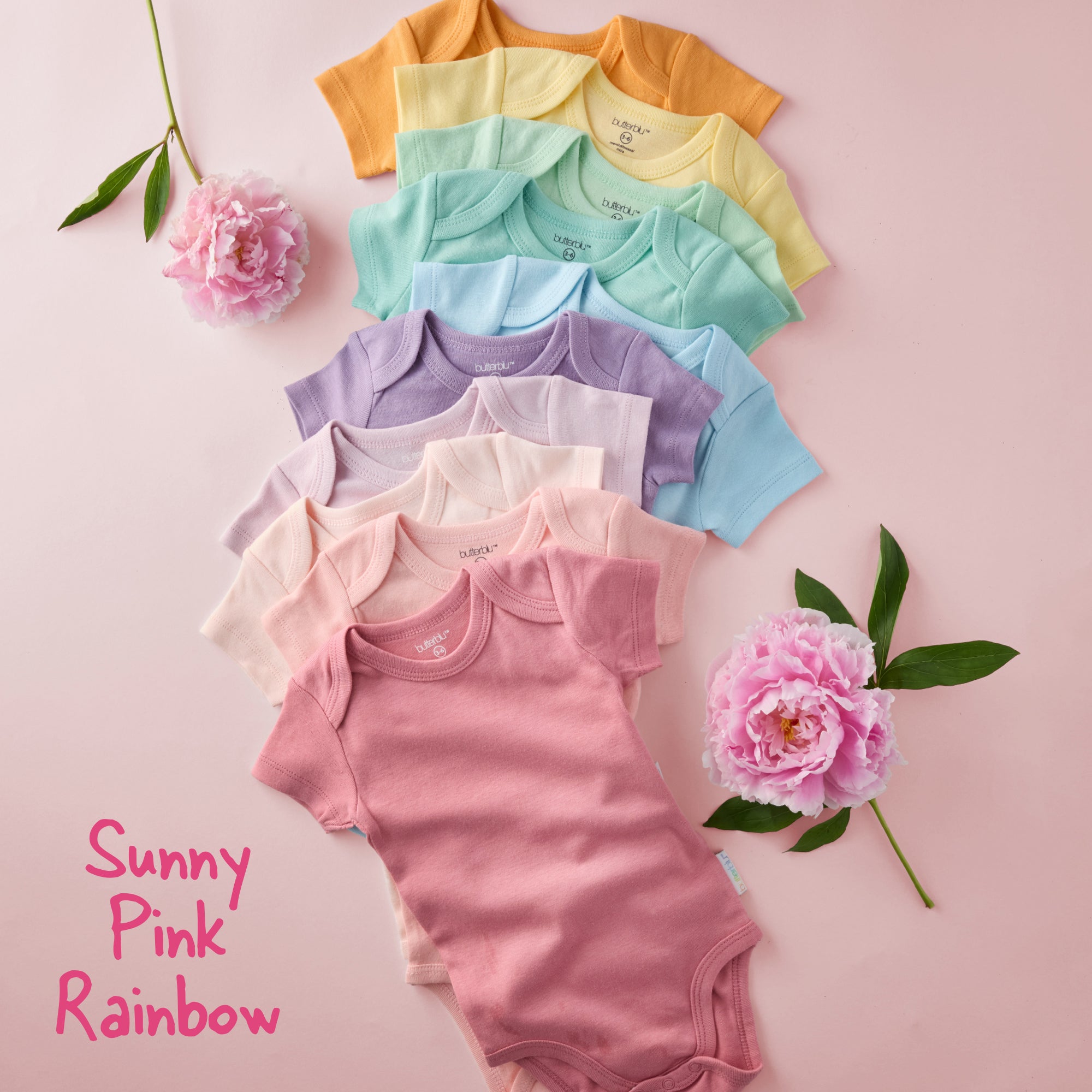 Colorful baby onesies arranged on a pink background with flowers.