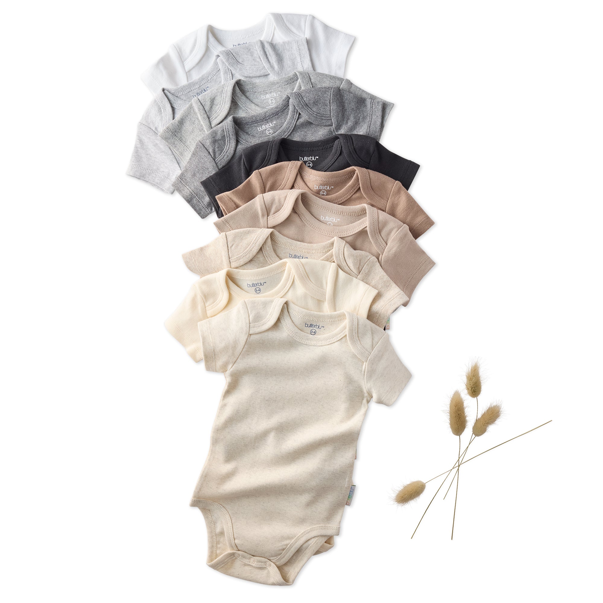 Stack of baby bodysuits in various colors on a white background with dried plants.