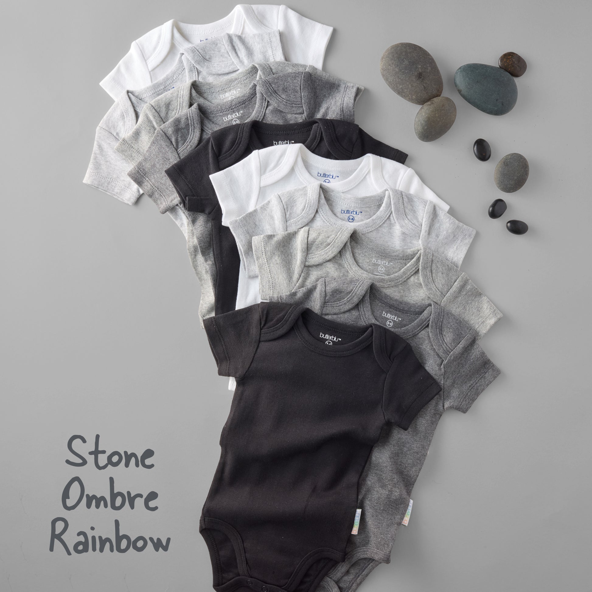 Stack of baby onesies in black, gray, and white on a gray background with stones.