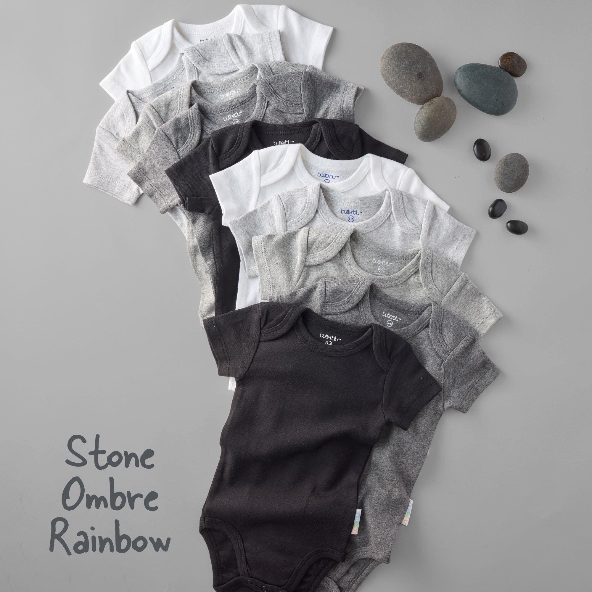 Stack of baby onesies in black, gray, and white on a gray background with stones.