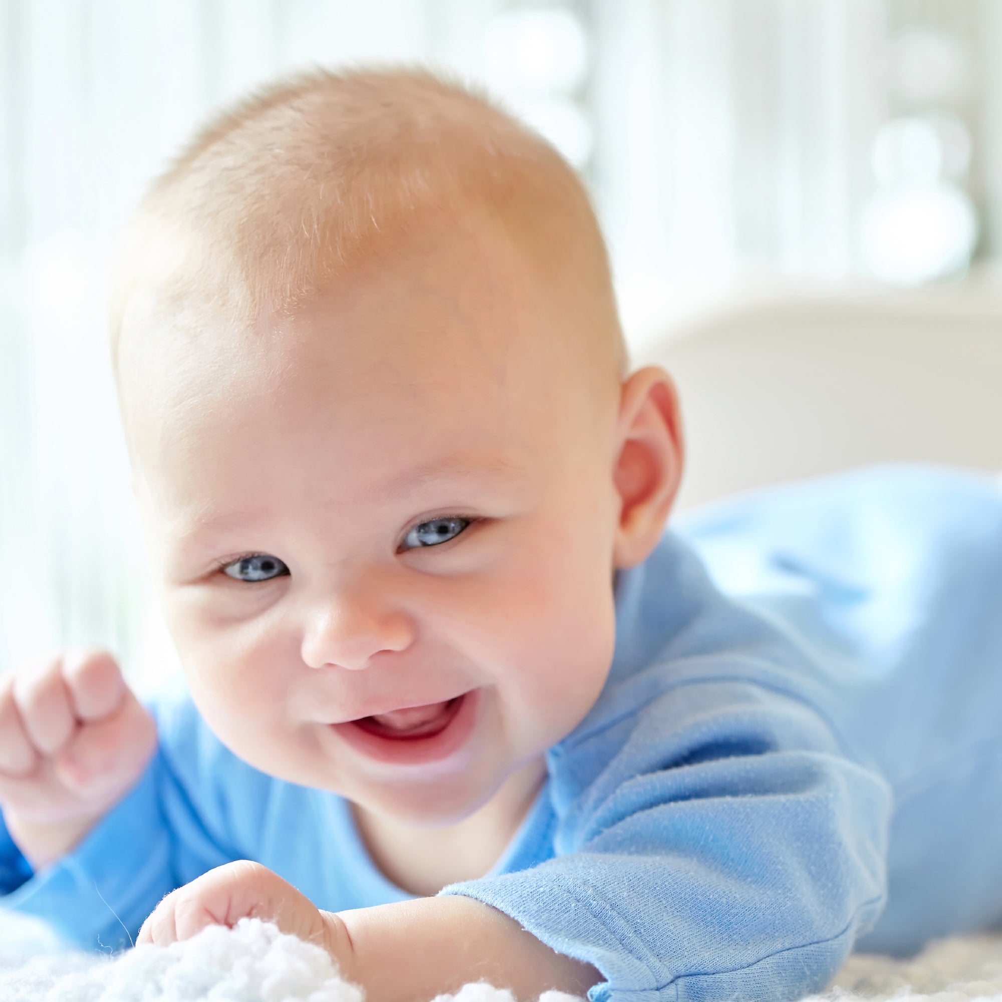 Baby in a blue outfit lying on a white surface with a blurred background