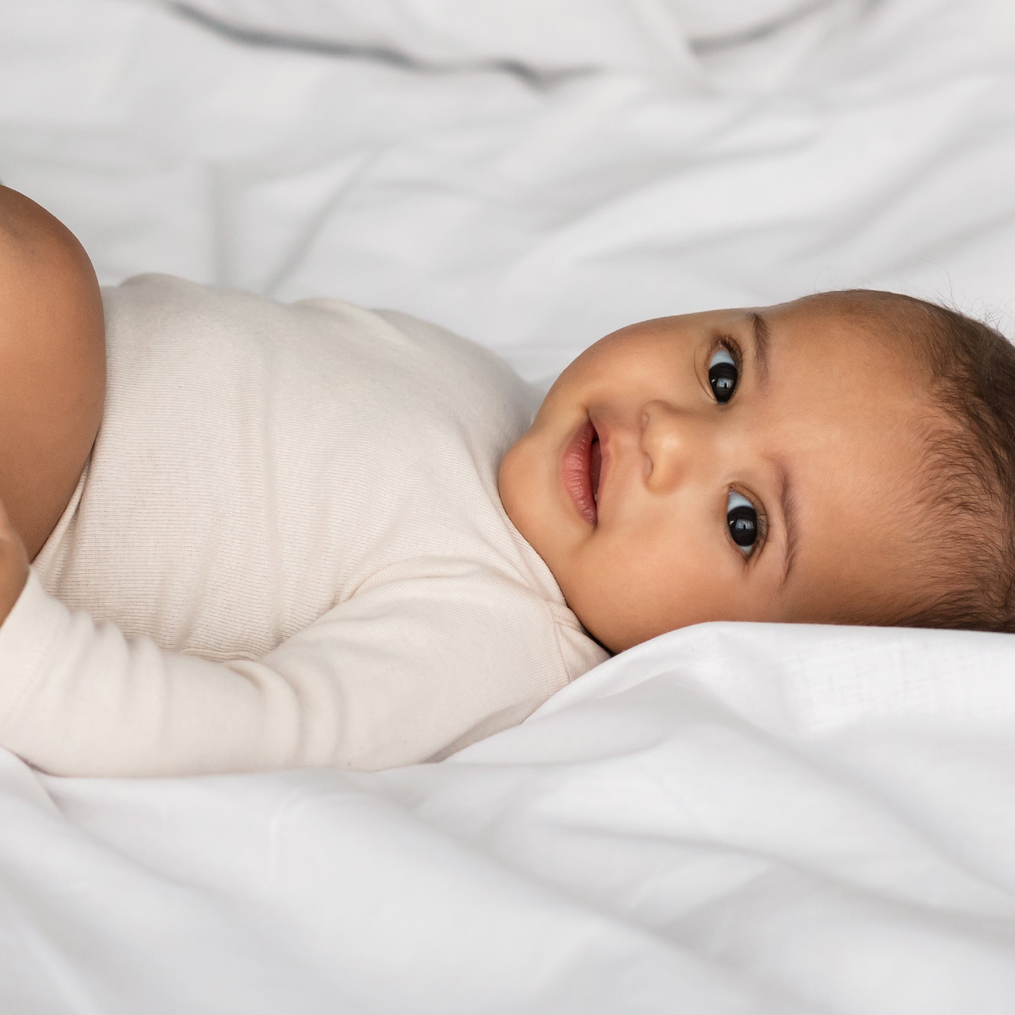Baby wrapped in a white blanket lying on a white surface