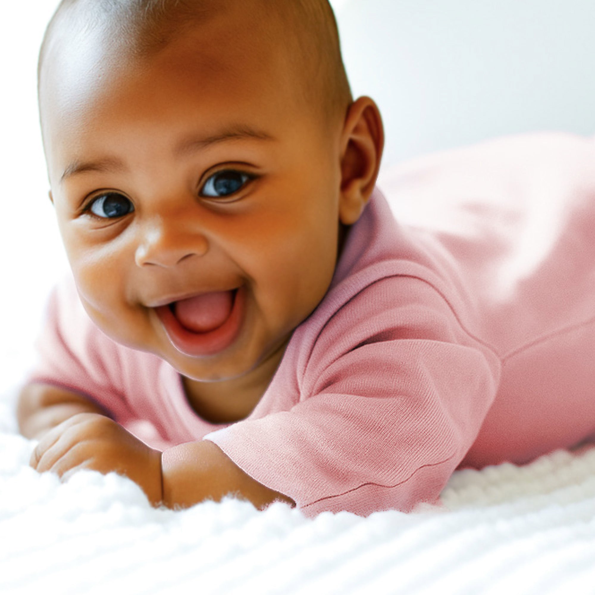 Baby in a pink outfit lying on a white surface
