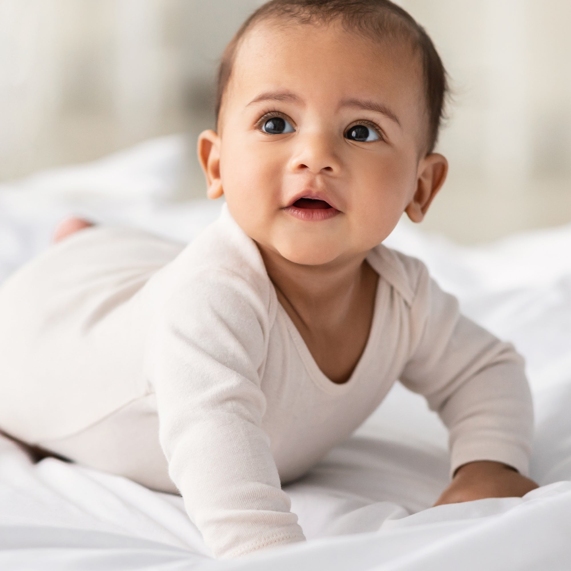 Baby wearing a white onesie lying on a white blanket