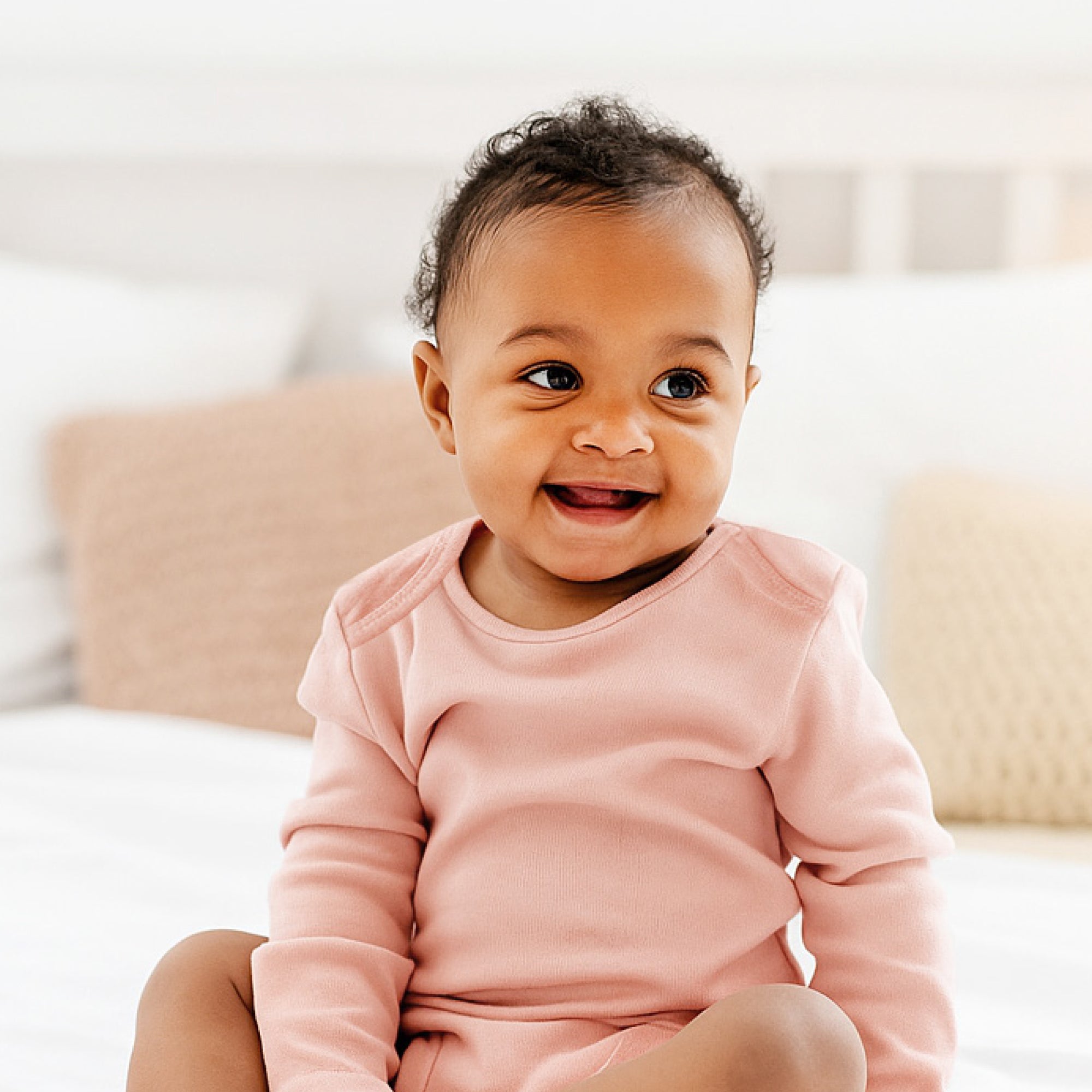 Baby in a pink outfit sitting on a couch with a blurred background
