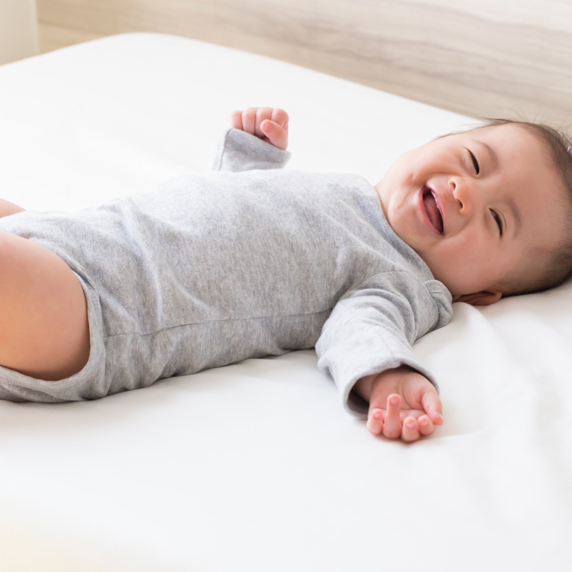 Baby in a gray onesie lying on a white surface