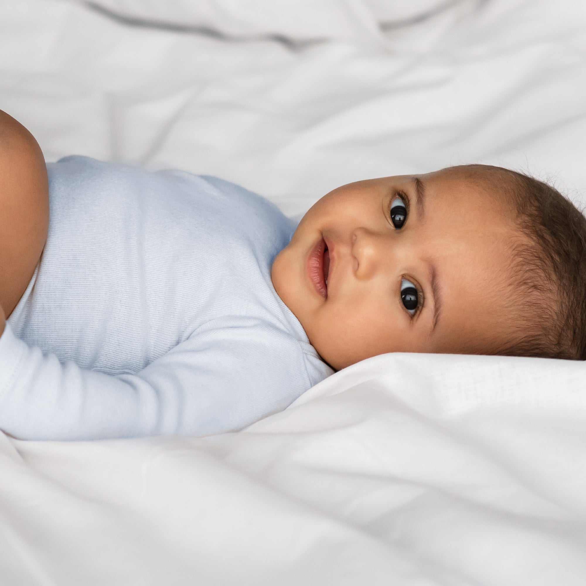 Baby in a light blue outfit lying on a white blanket