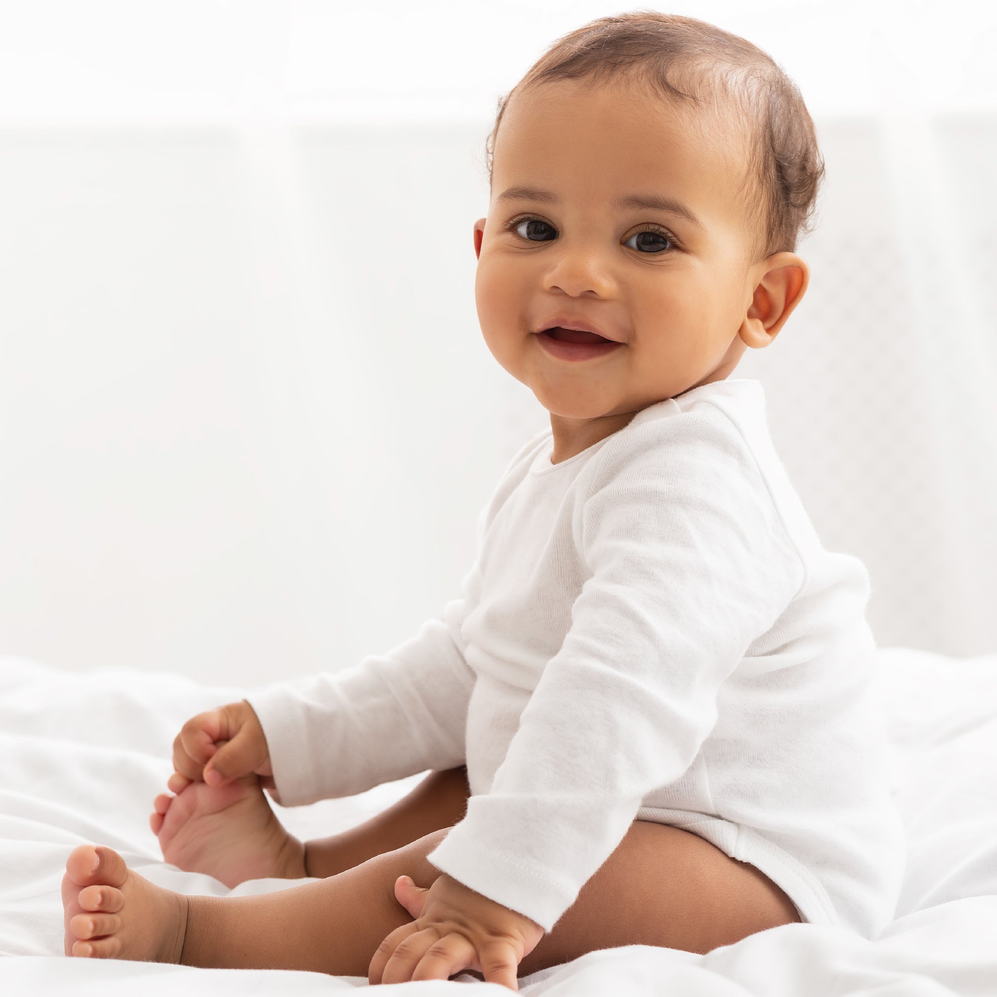 Baby in a white onesie sitting on a white surface