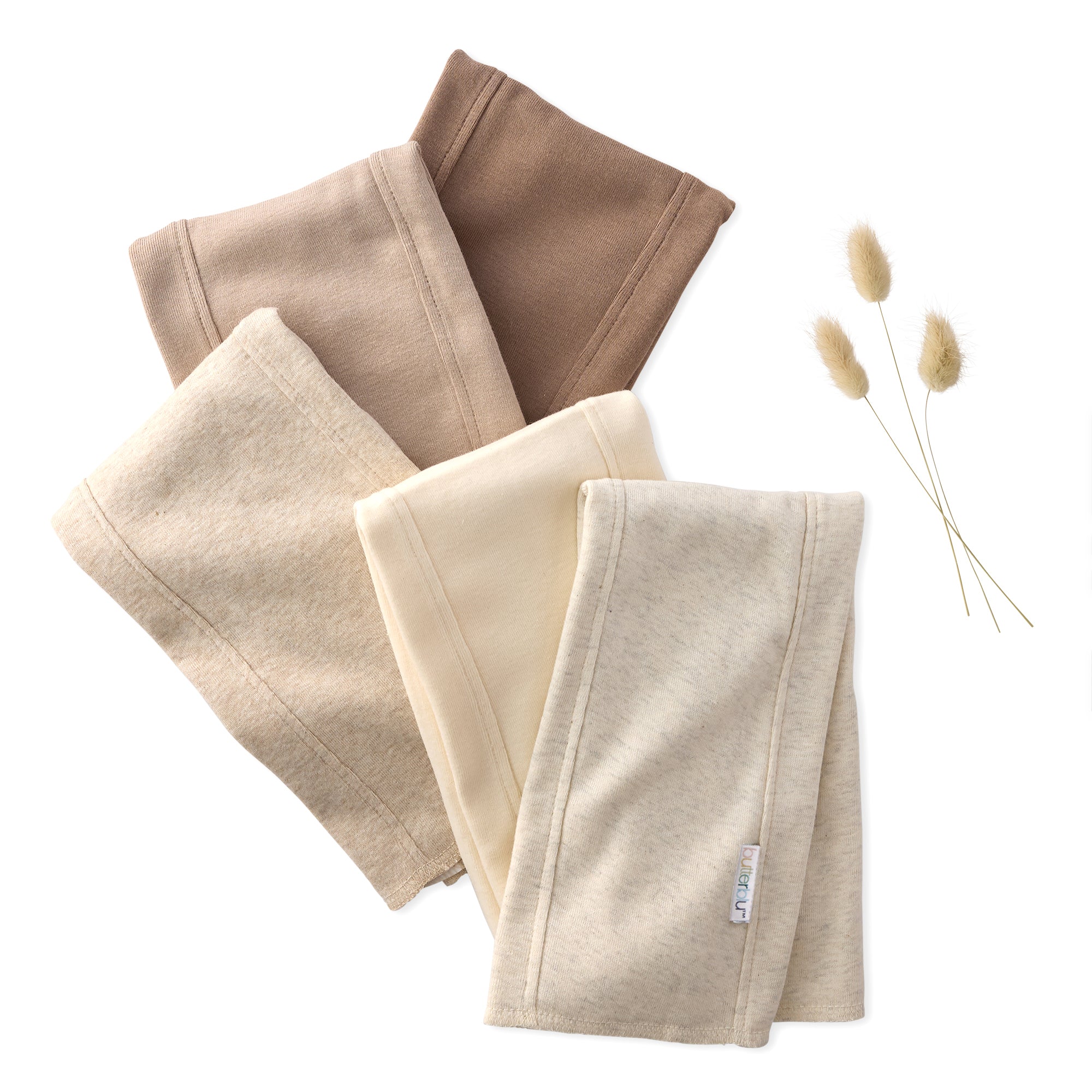 Set of folded BAILEY Burp Cloths in beige and brown on a white background with dried herbs.