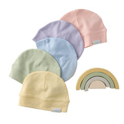Set of pastel-colored baby hats and a rainbow toy on a white background