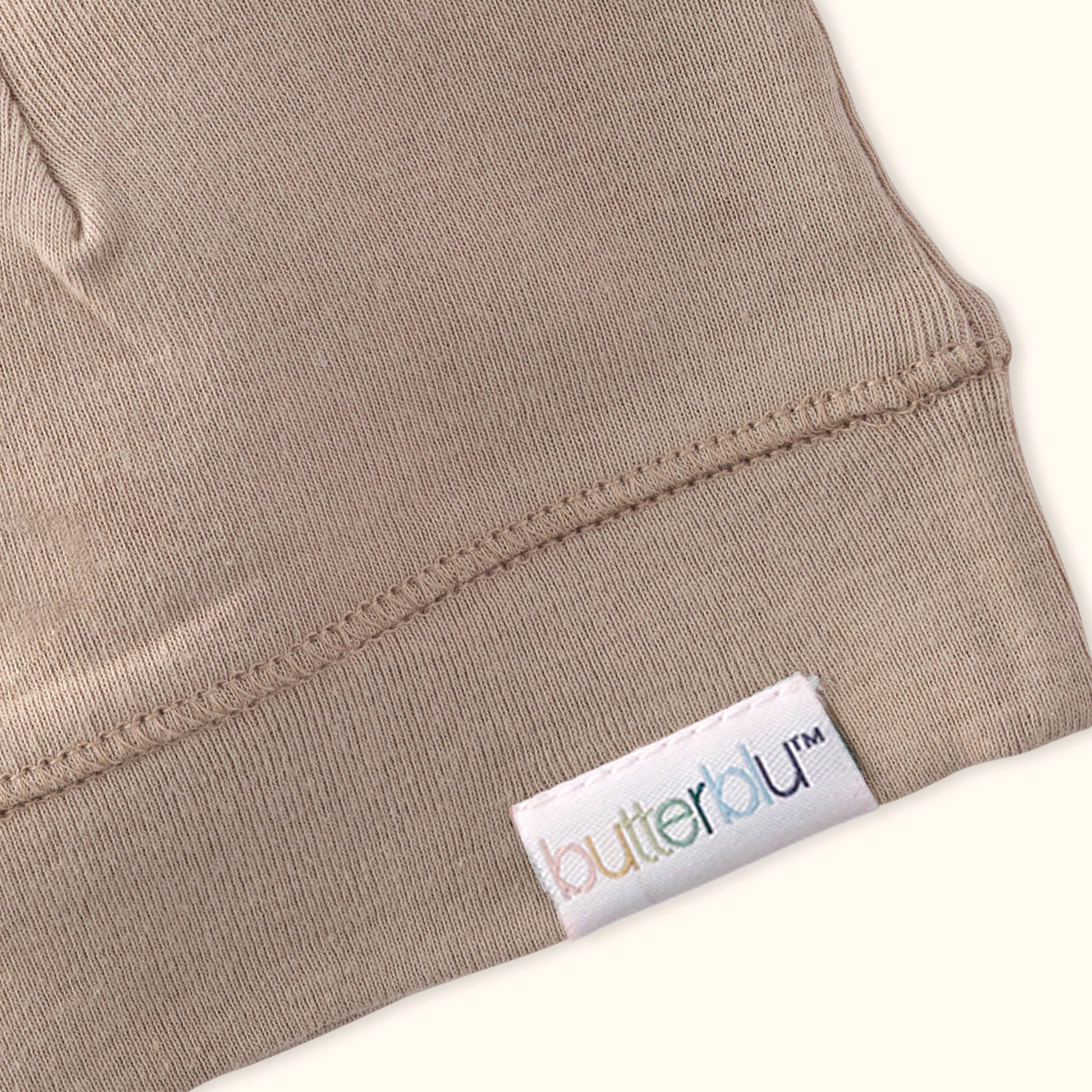 Close-up of a beige garment with a 'butterfly' brand label on a white background