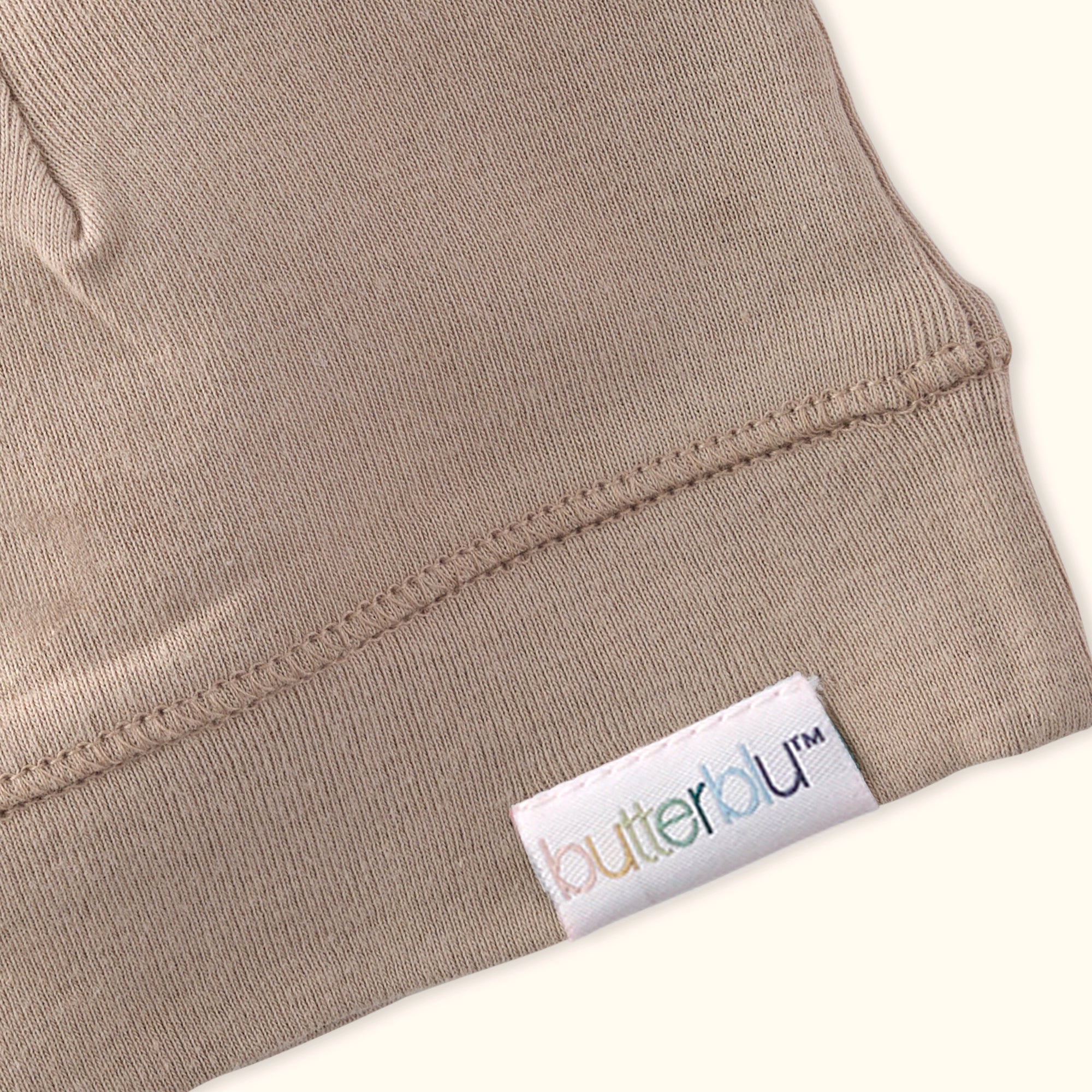 Close-up of a beige garment with a 'butterfly' brand label on a white background