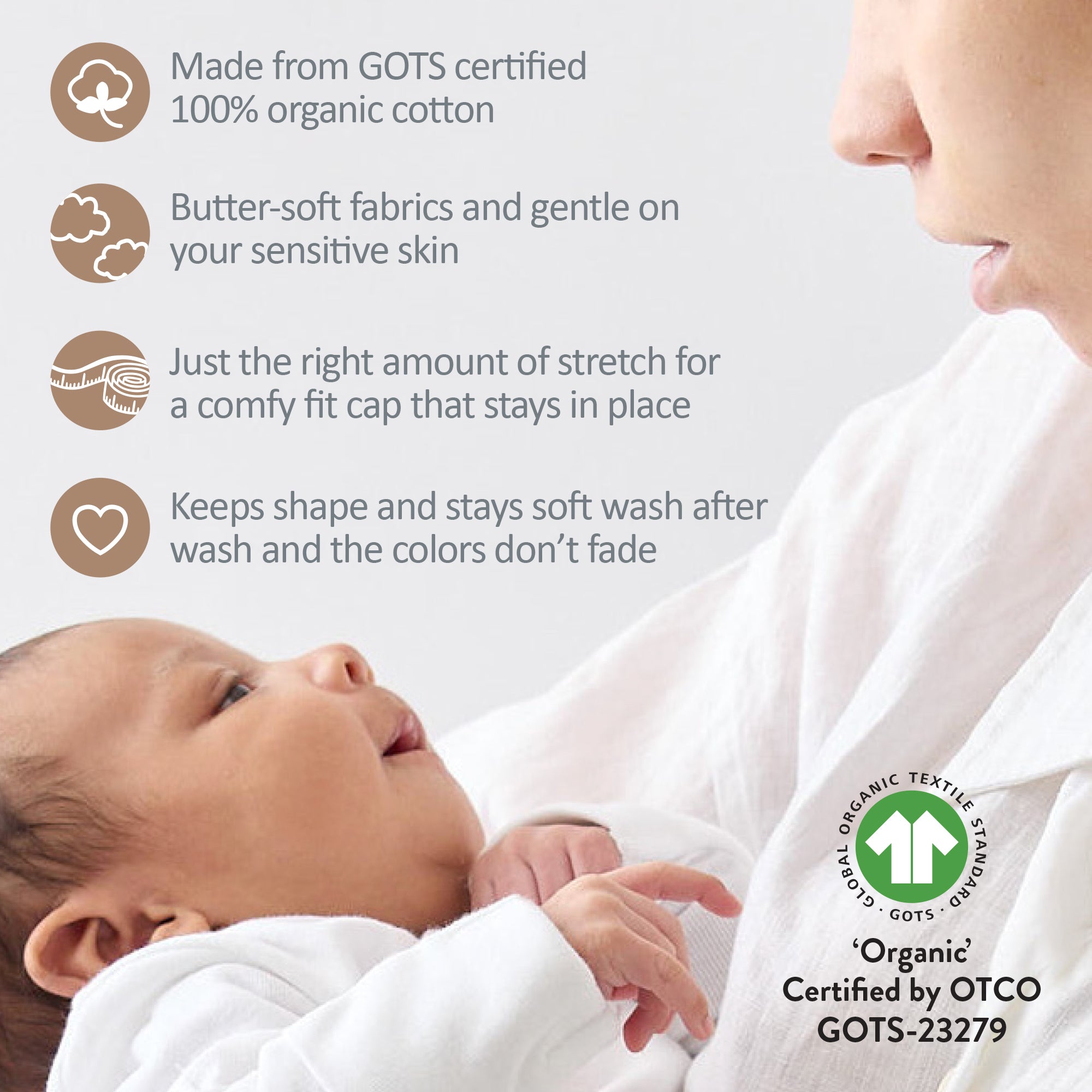 Baby wearing a white cap with text about organic cotton and GOTS certification, next to a person holding the baby.