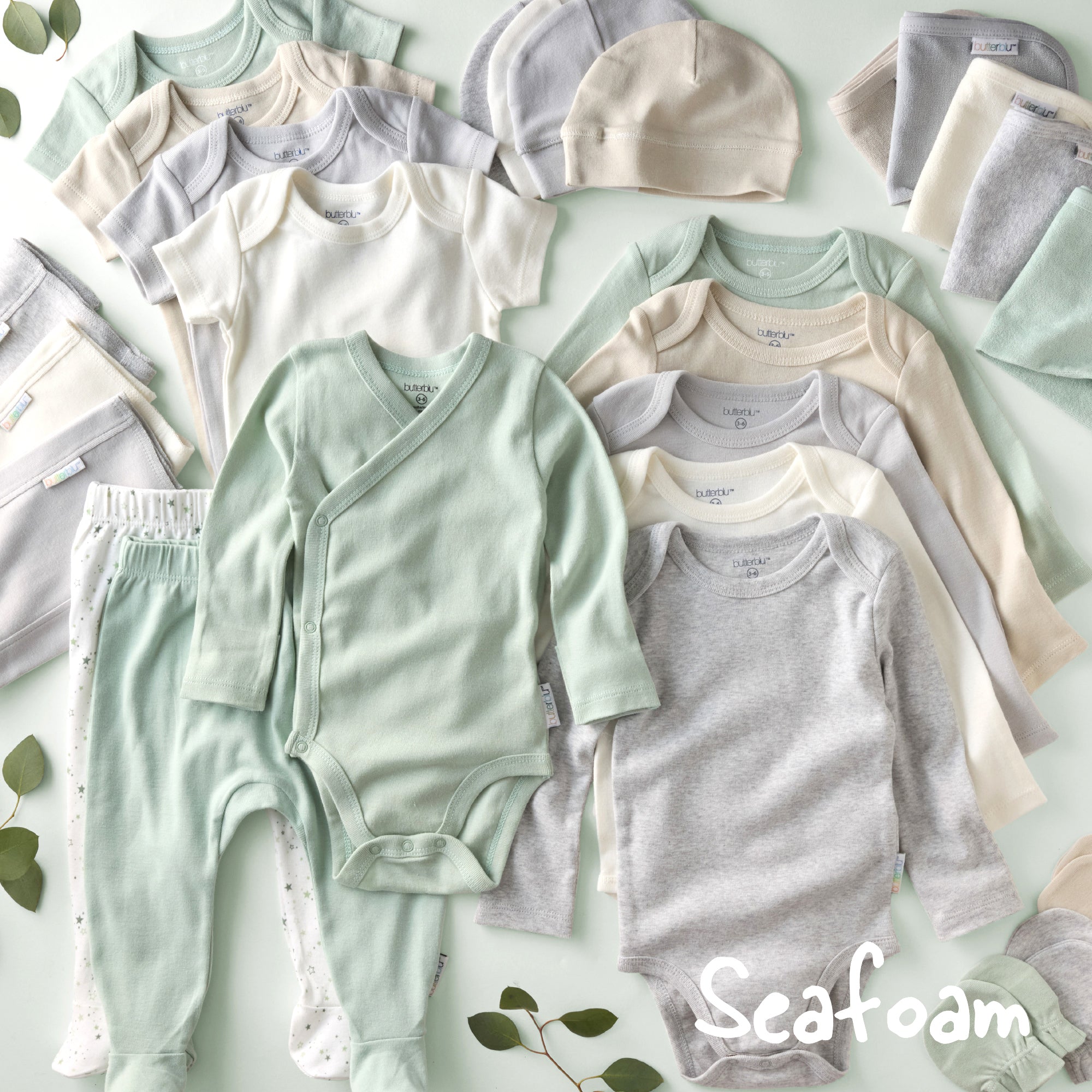 Collection of baby clothes in seafoam green, gray, and beige on a light green background.