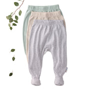 Three pairs of baby pants in green, beige, and gray on a white background with a branch and leaves.