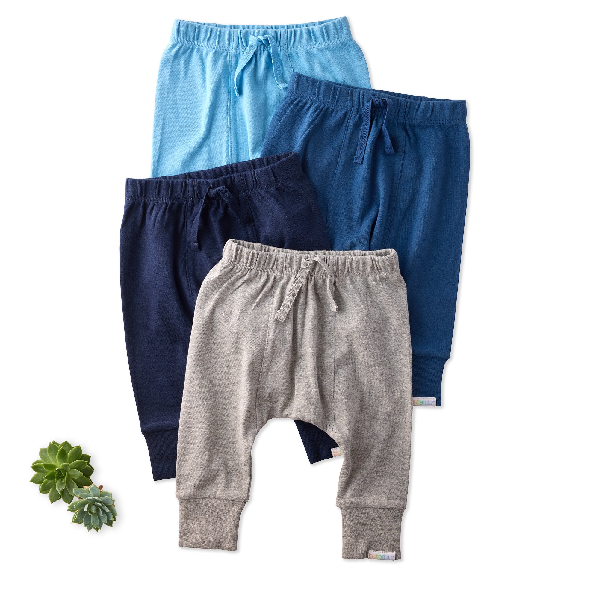Three pairs of children's pants in blue, gray, and navy on a white background with a succulent plant.