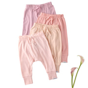 Three pairs of pink baby pants stacked on a white background with a flower.