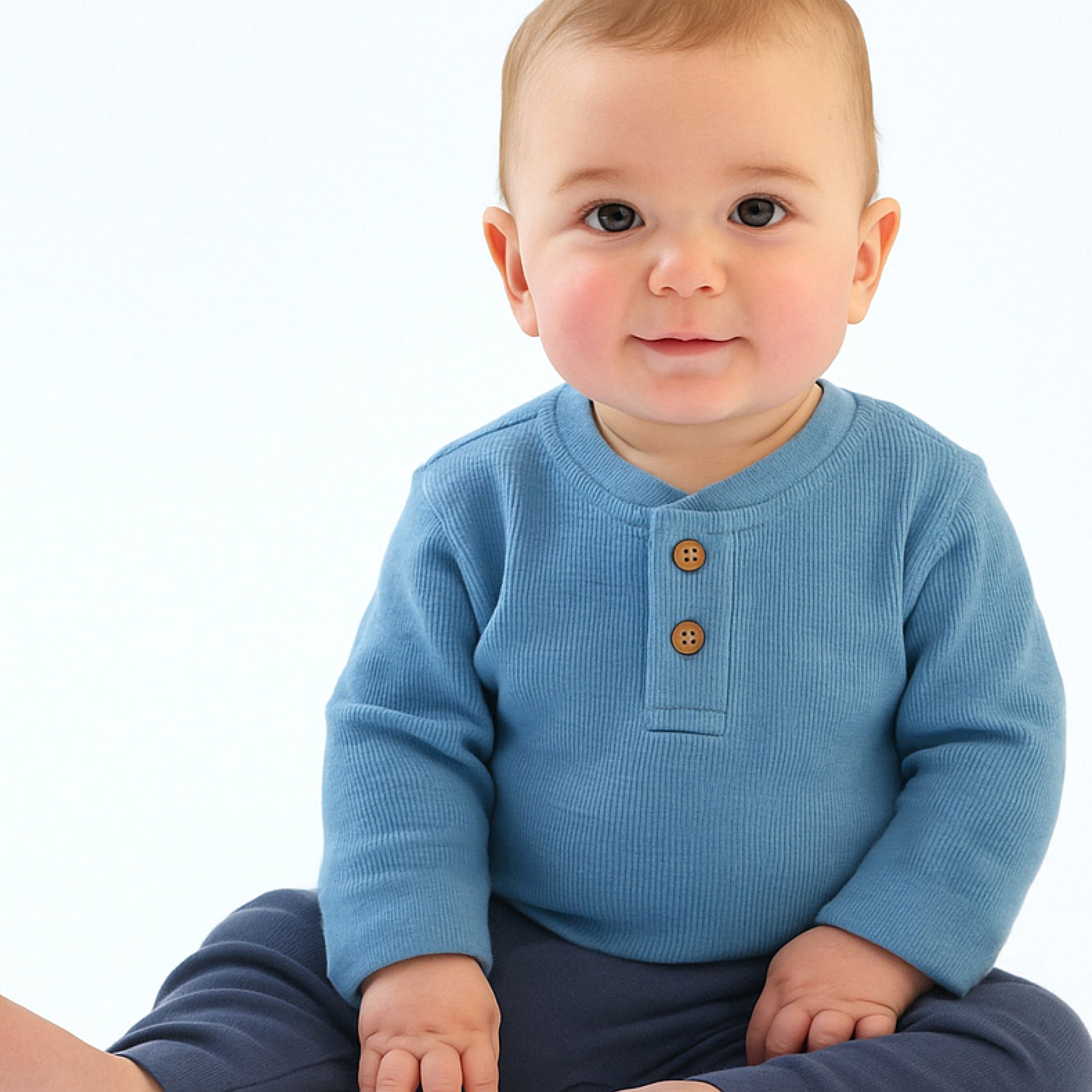 Baby wearing a blue long-sleeve shirt with brown buttons on a white background