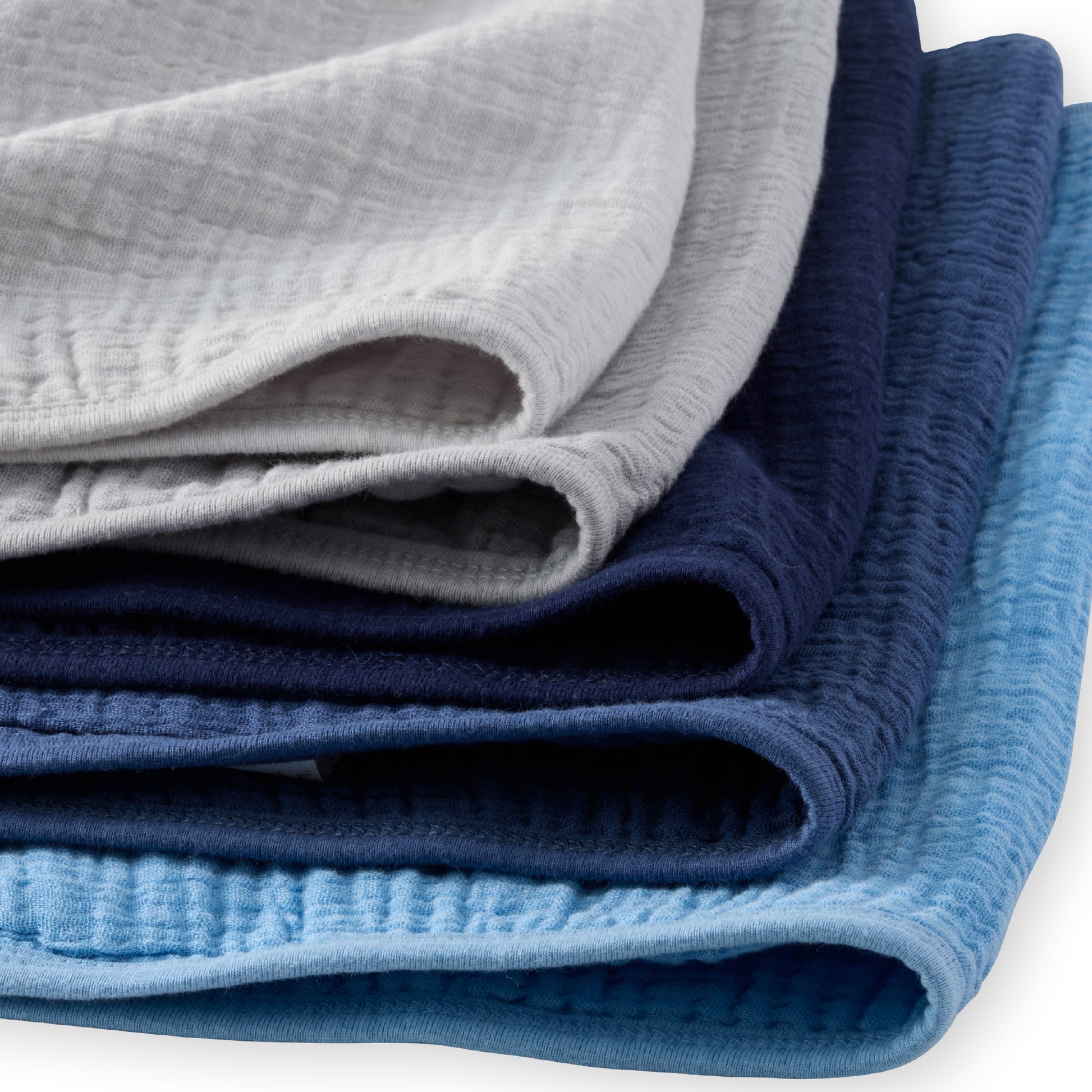 Stack of folded textured fabric sheets in gray, blue, and navy on a white background