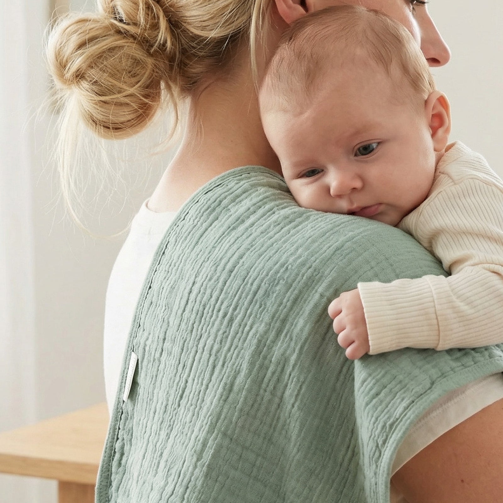 Woman holding a baby close, wearing a green textured burp cloth