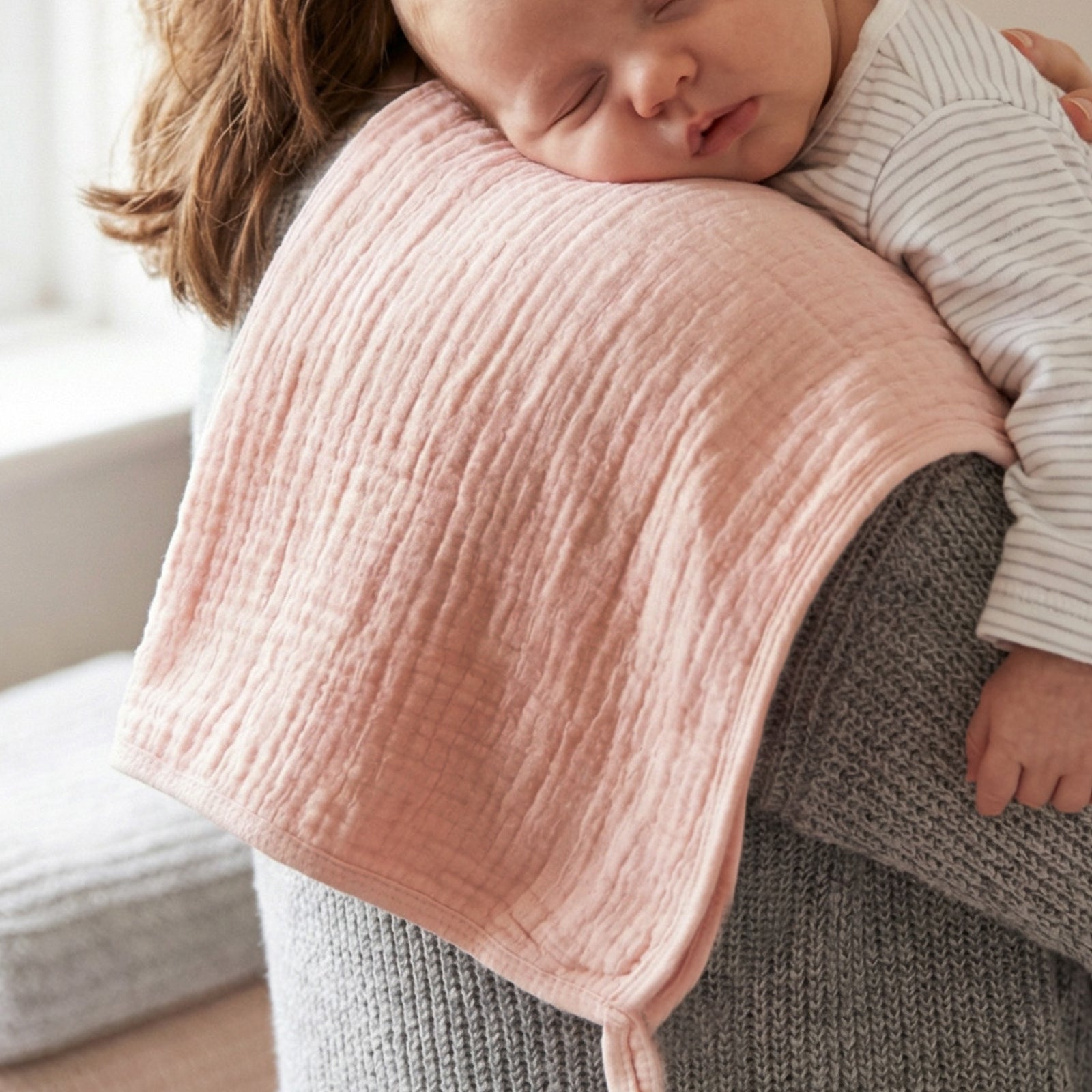 Person holding a baby wrapped in a pink blanket with a blurred background