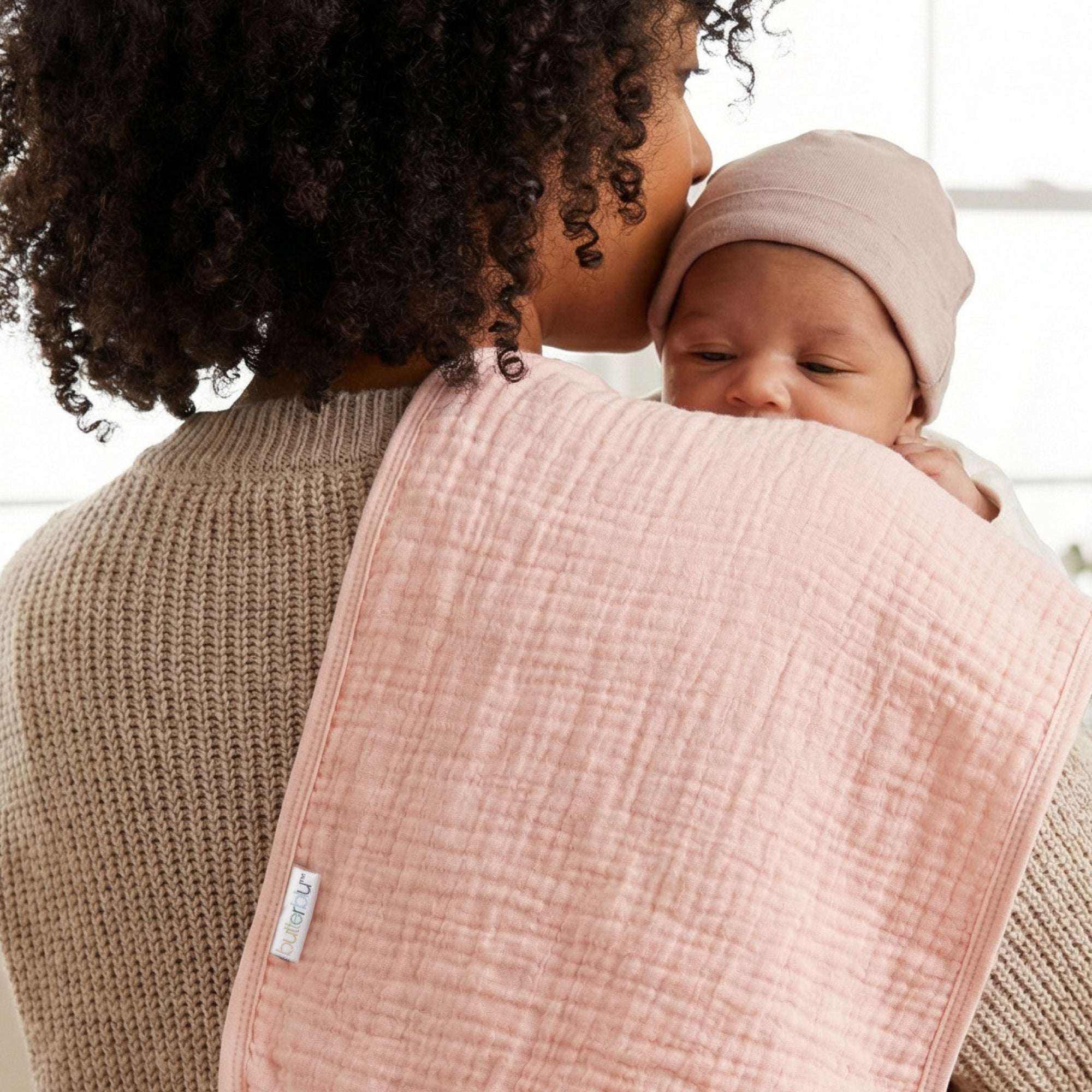Woman holding a baby wrapped in a pink blanket with a blurred background