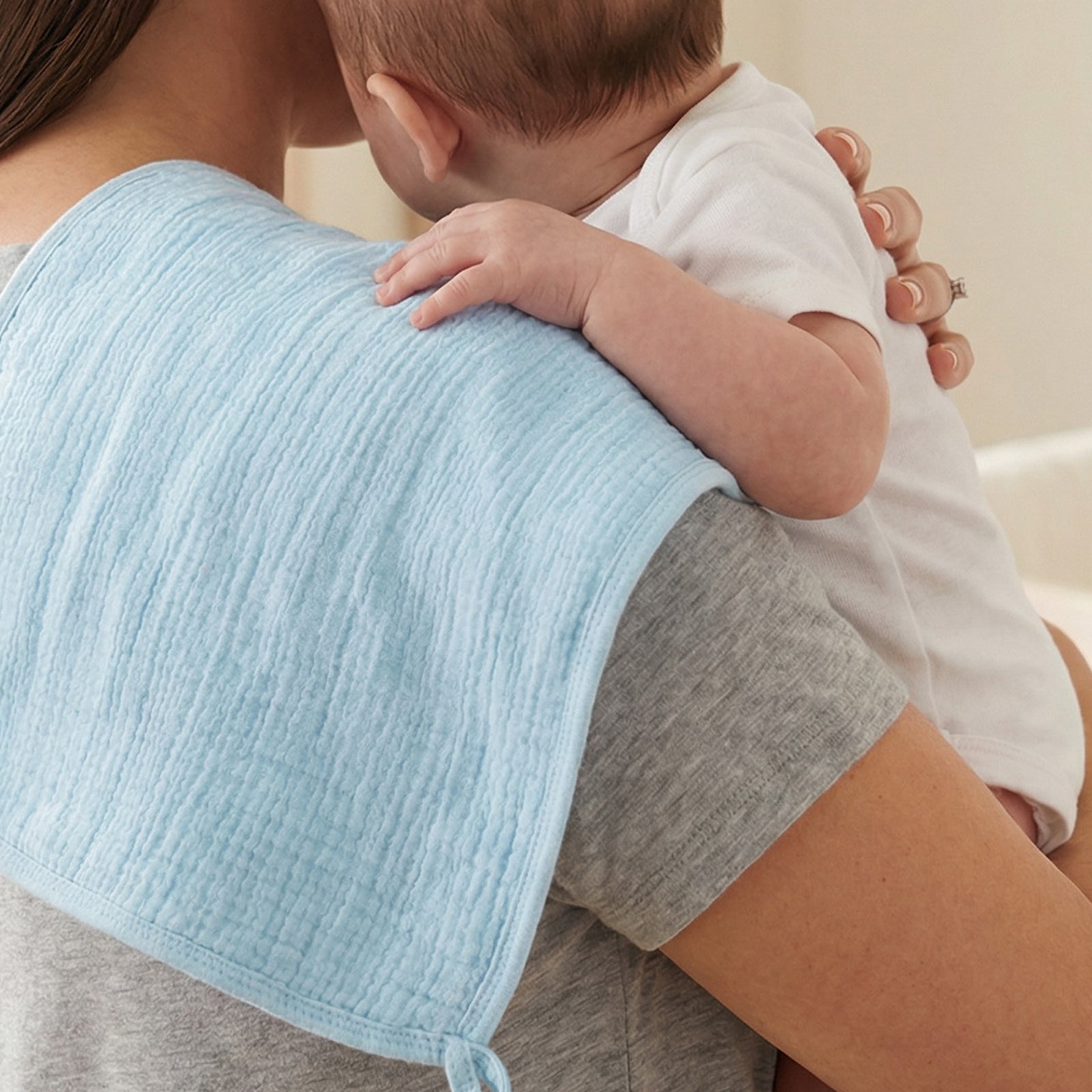 Person holding a baby with a blue textured blanket draped over their shoulder.