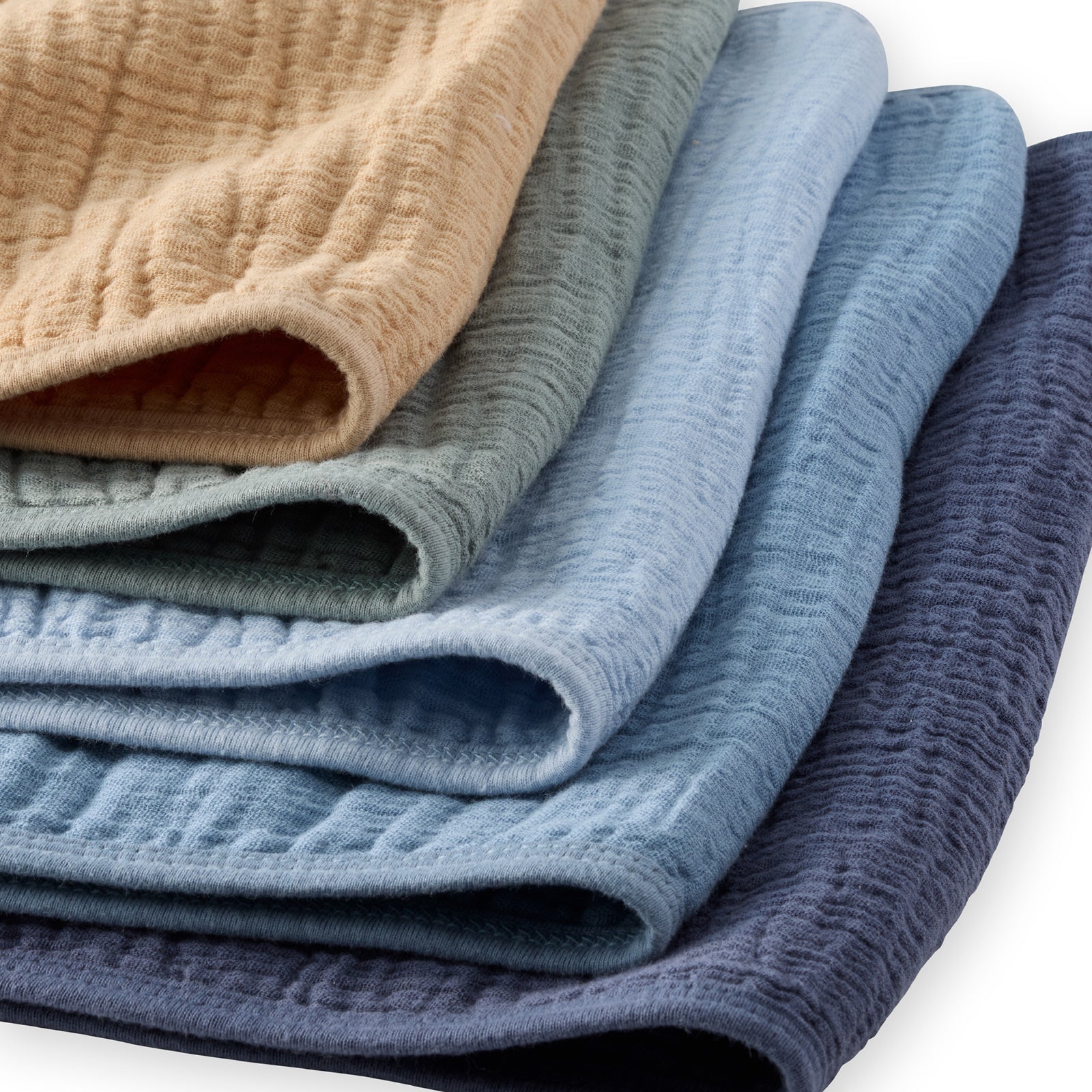 Stack of folded textured fabric in beige, green, blue, and purple on a white background