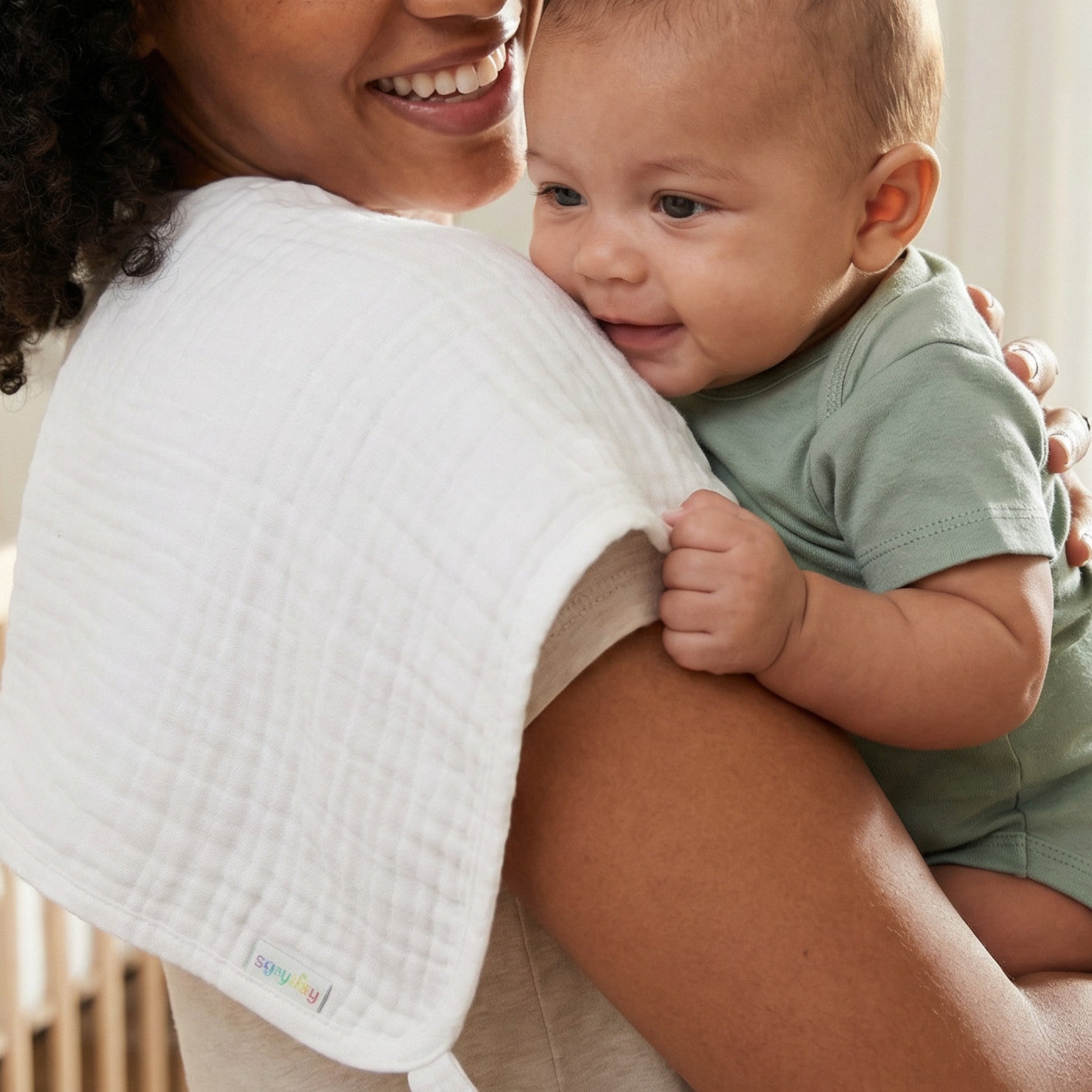 Woman holding a baby wearing a green onesie with a white bib.
