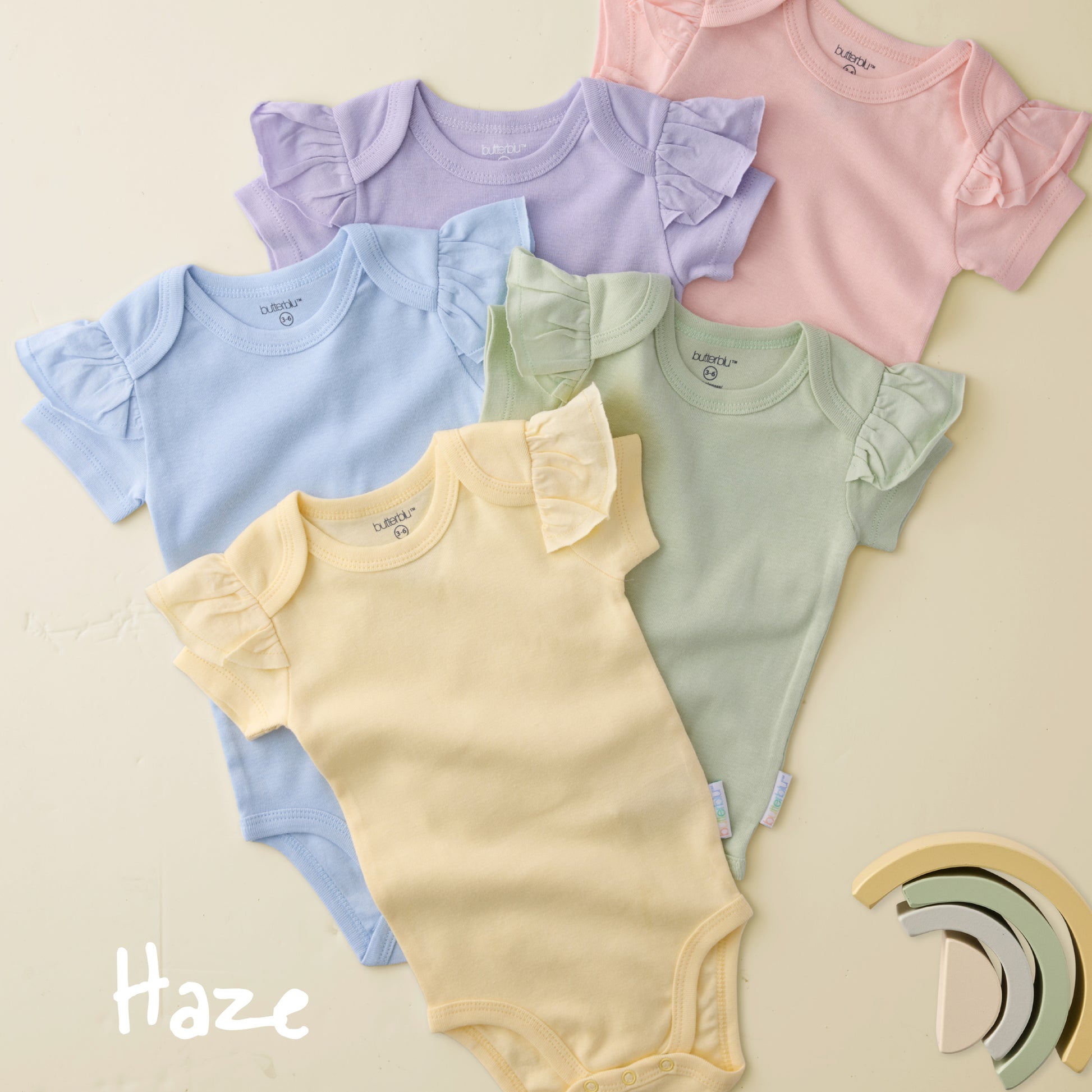 Set of colorful baby bodysuits with ruffled sleeves on a beige background