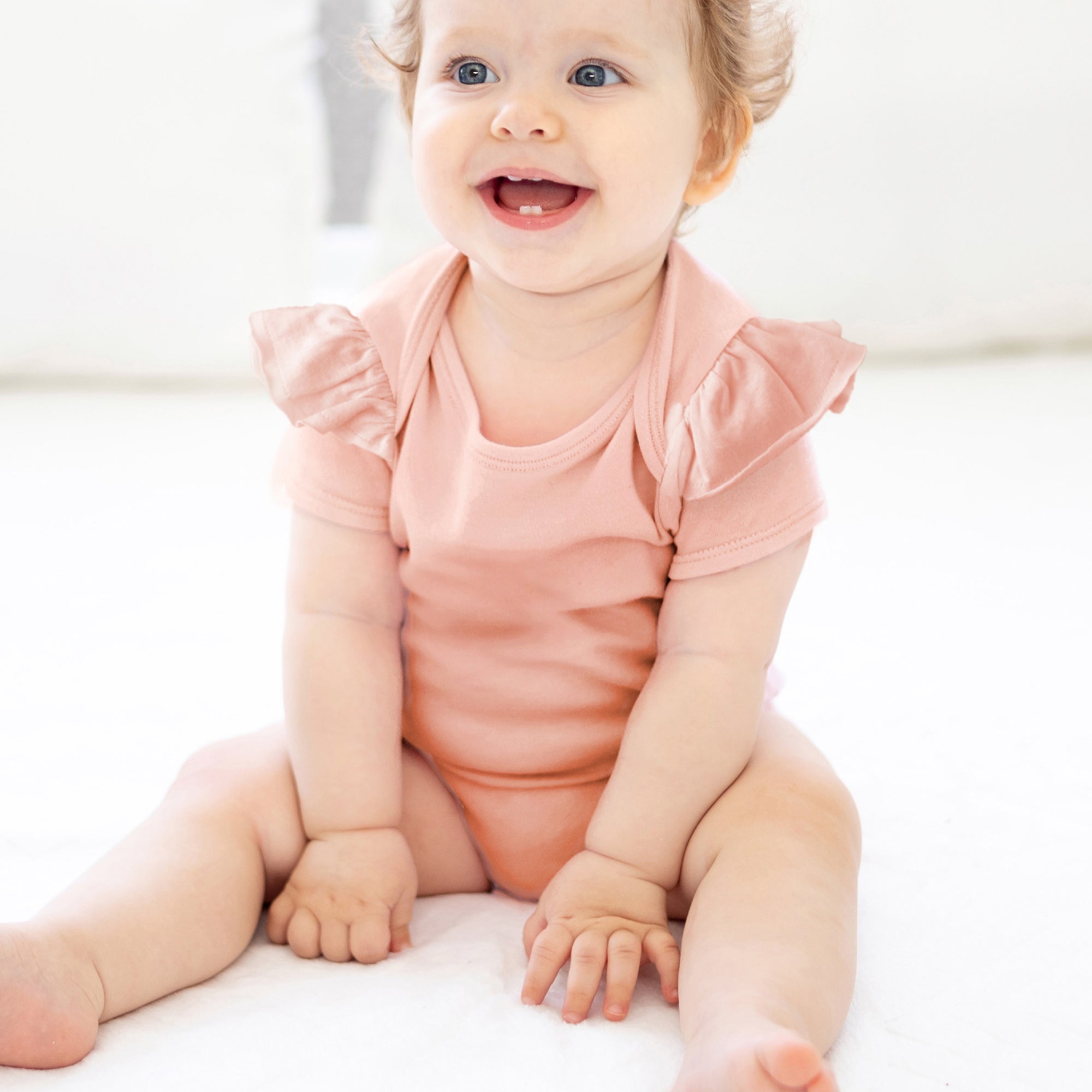 Baby wearing a pink onesie sitting on a white surface