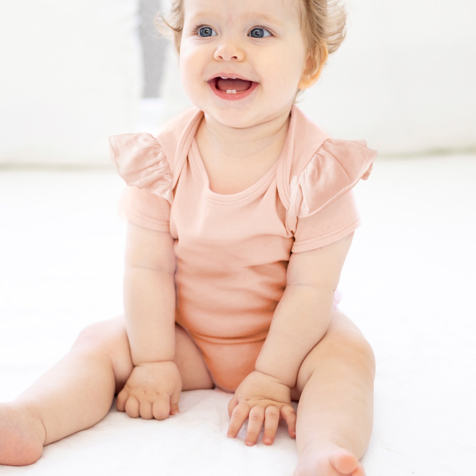 Baby wearing a pink onesie sitting on a white surface