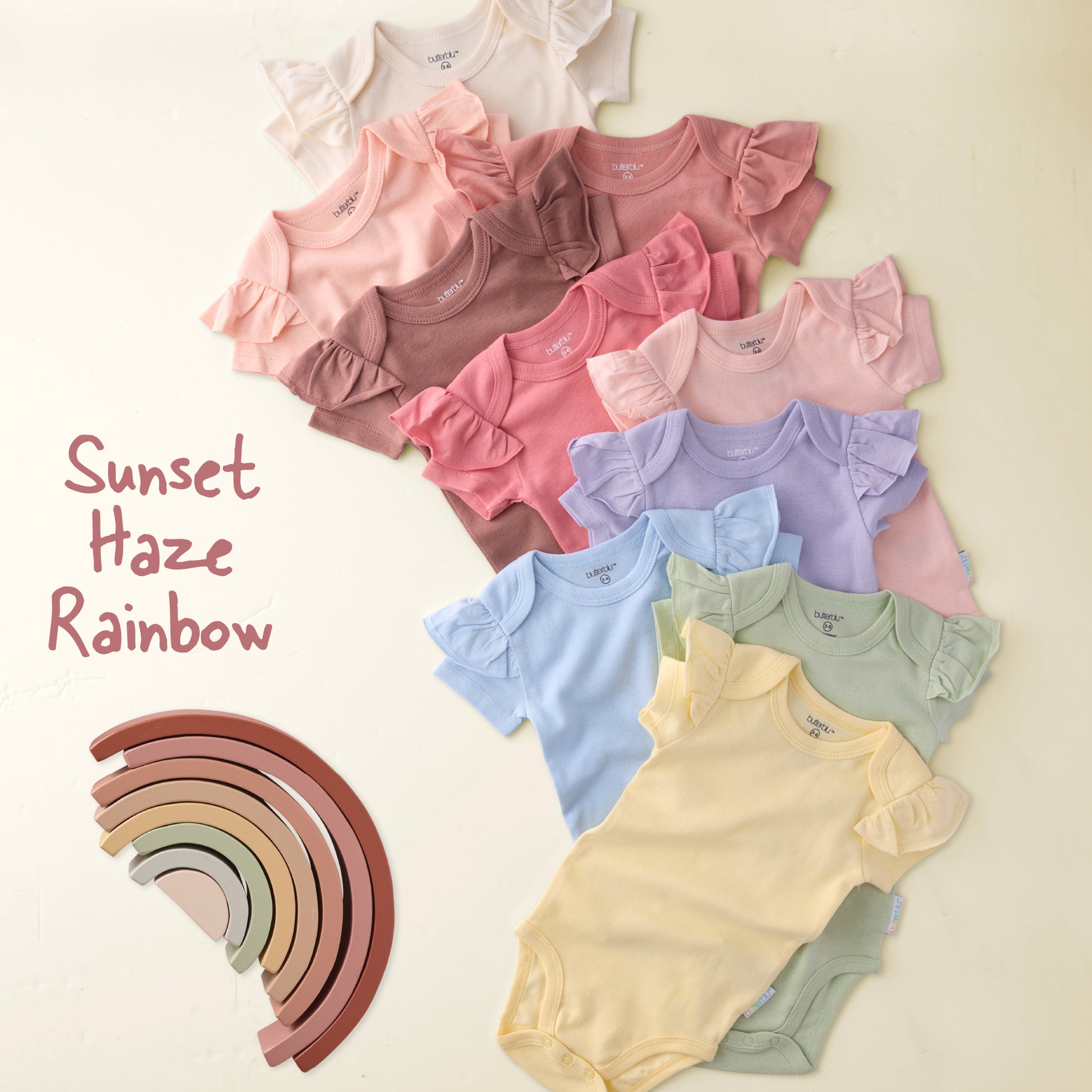 Colorful baby rompers in a rainbow pattern with a wooden rainbow toy on a beige background.