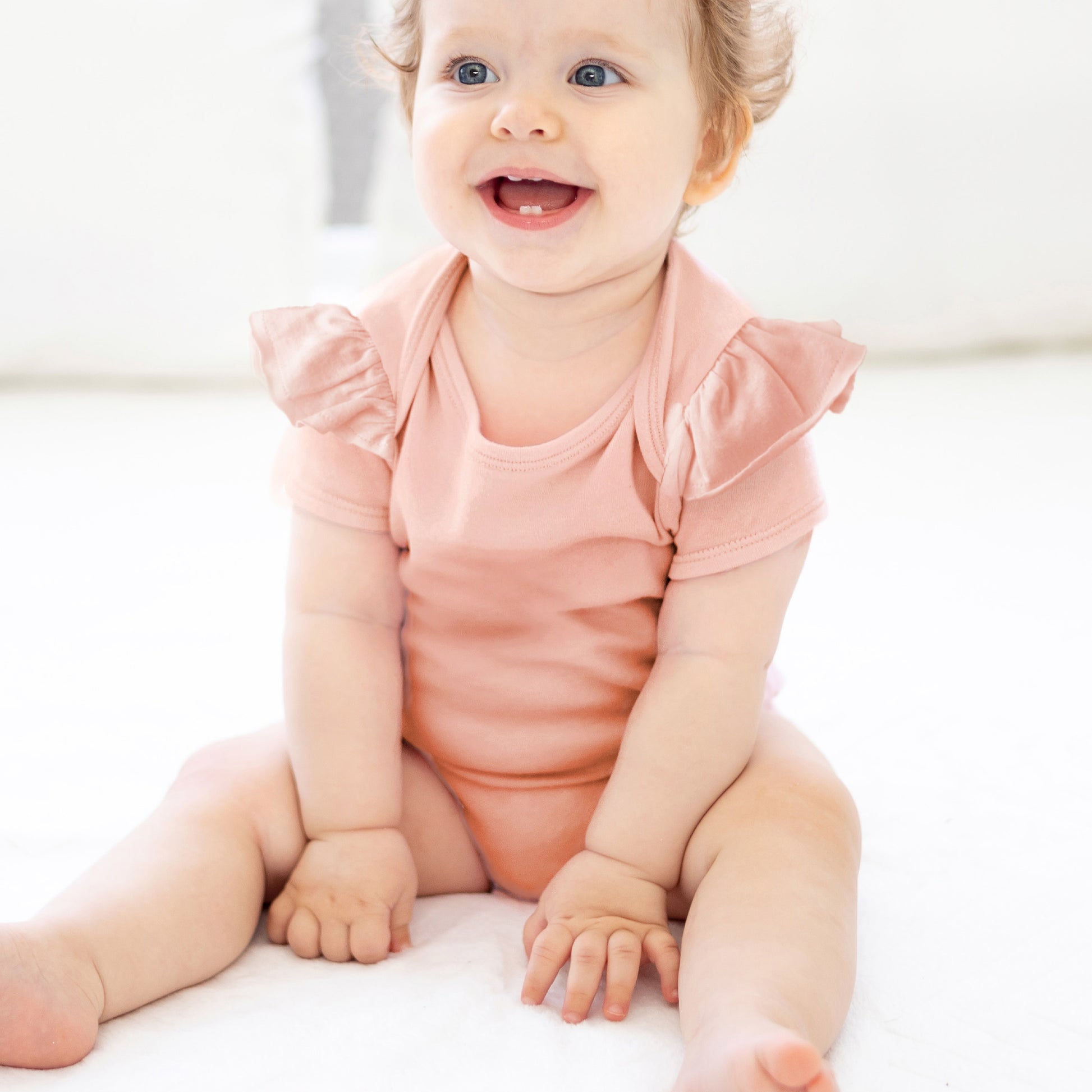 Baby wearing a pink onesie sitting on a white surface