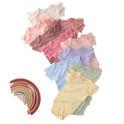 Stack of colorful baby bodysuits with a wooden rainbow toy on a white background