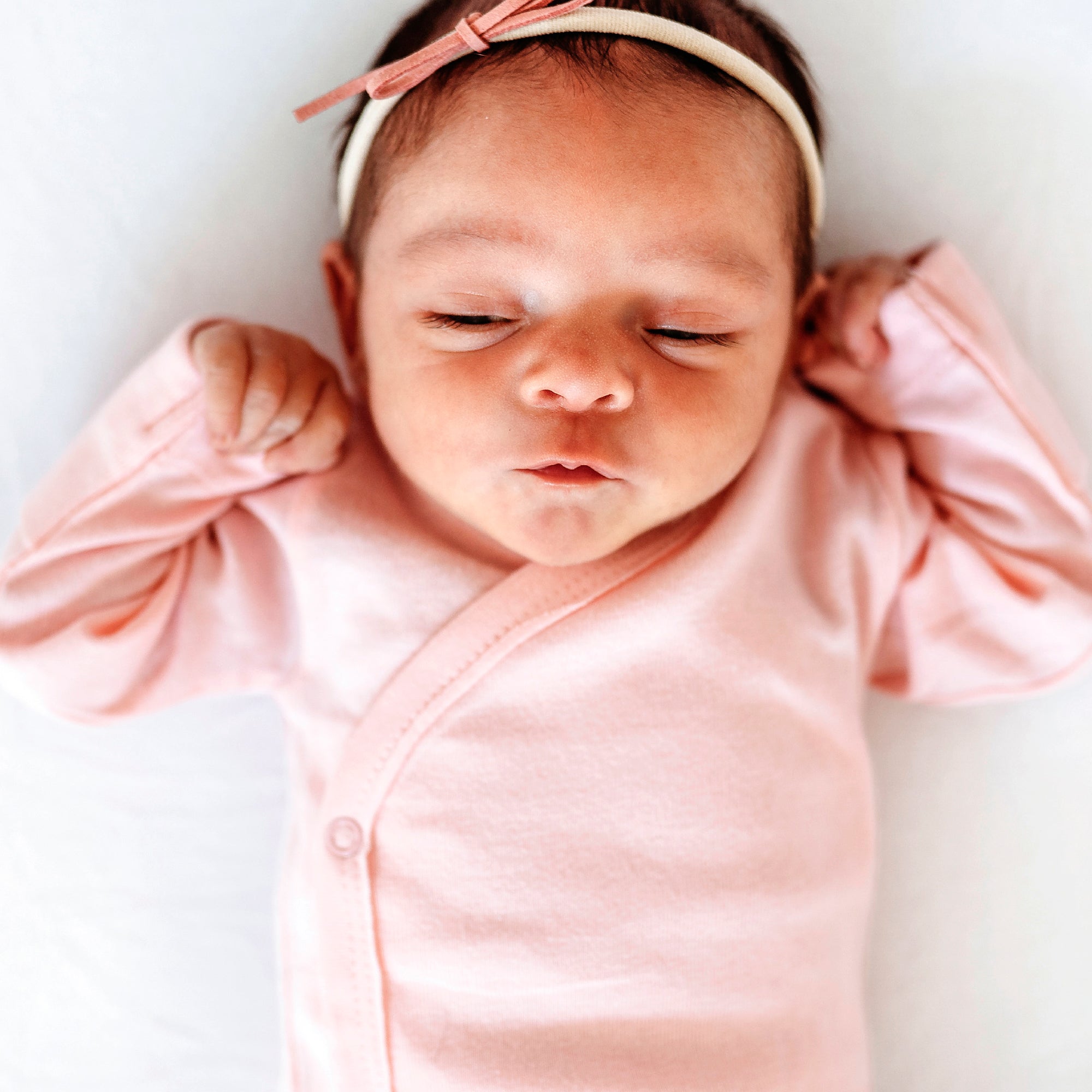 Newborn baby in a pink outfit with a matching headband on a white background