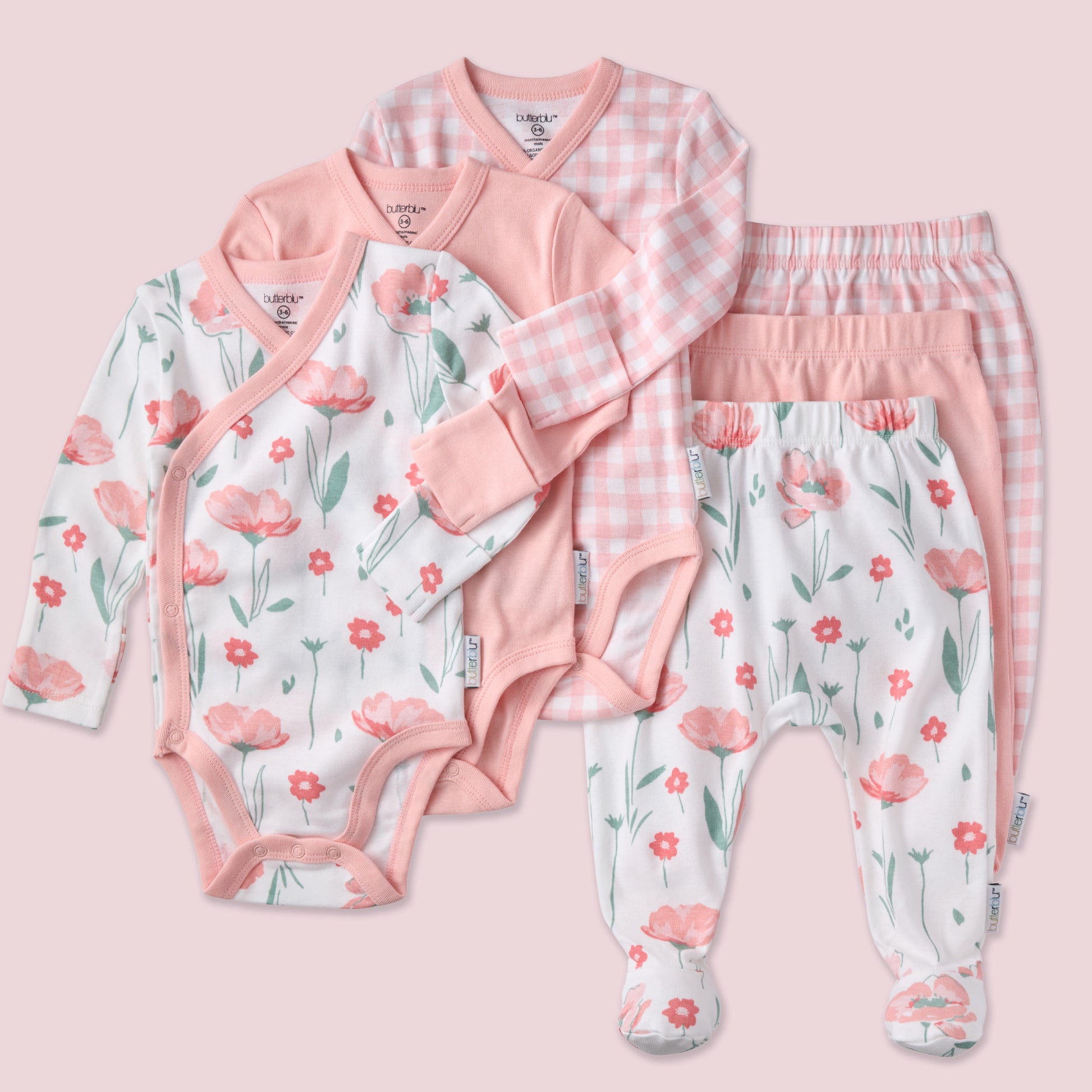Set of baby clothing including a onesie, shirt, and pants with floral patterns on a pink background.