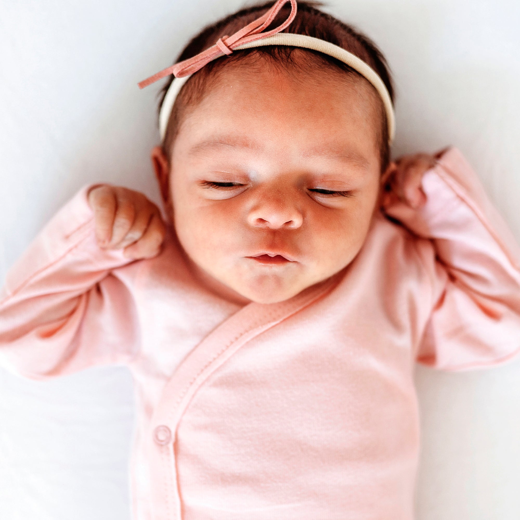 Newborn baby wearing a pink outfit and headband on a white background