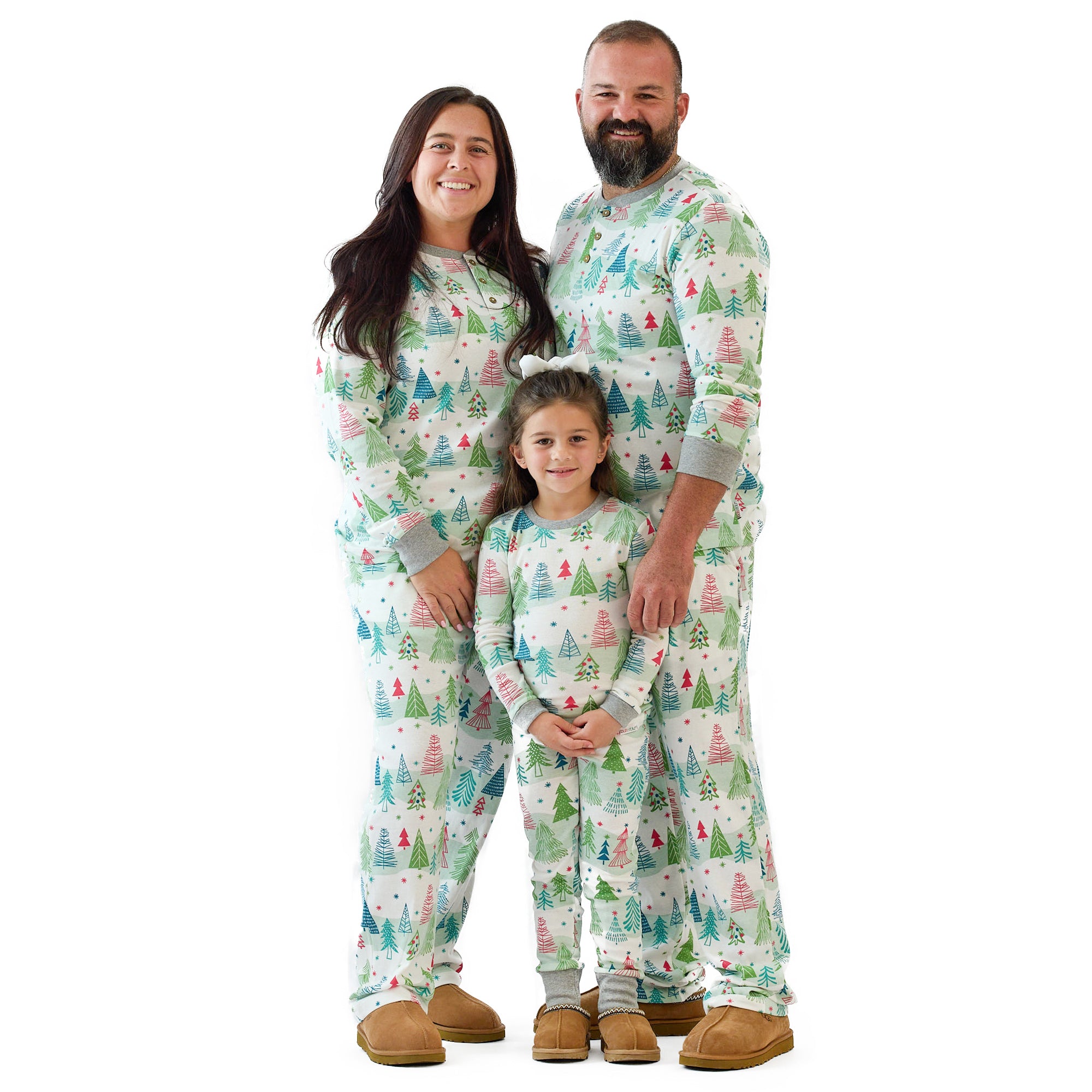 Family of three wearing matching pajamas with a Christmas tree pattern on a white background
