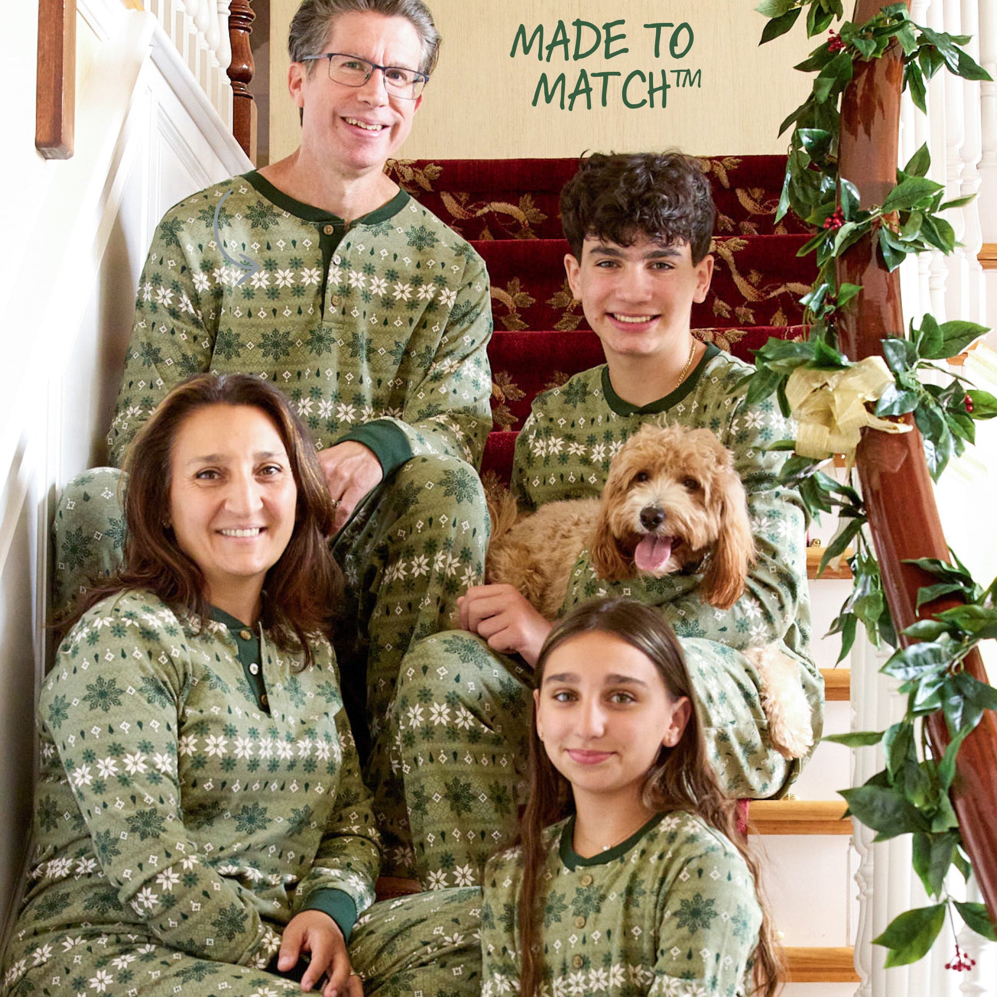 Family of four in matching green pajamas with a dog, sitting on a staircase.