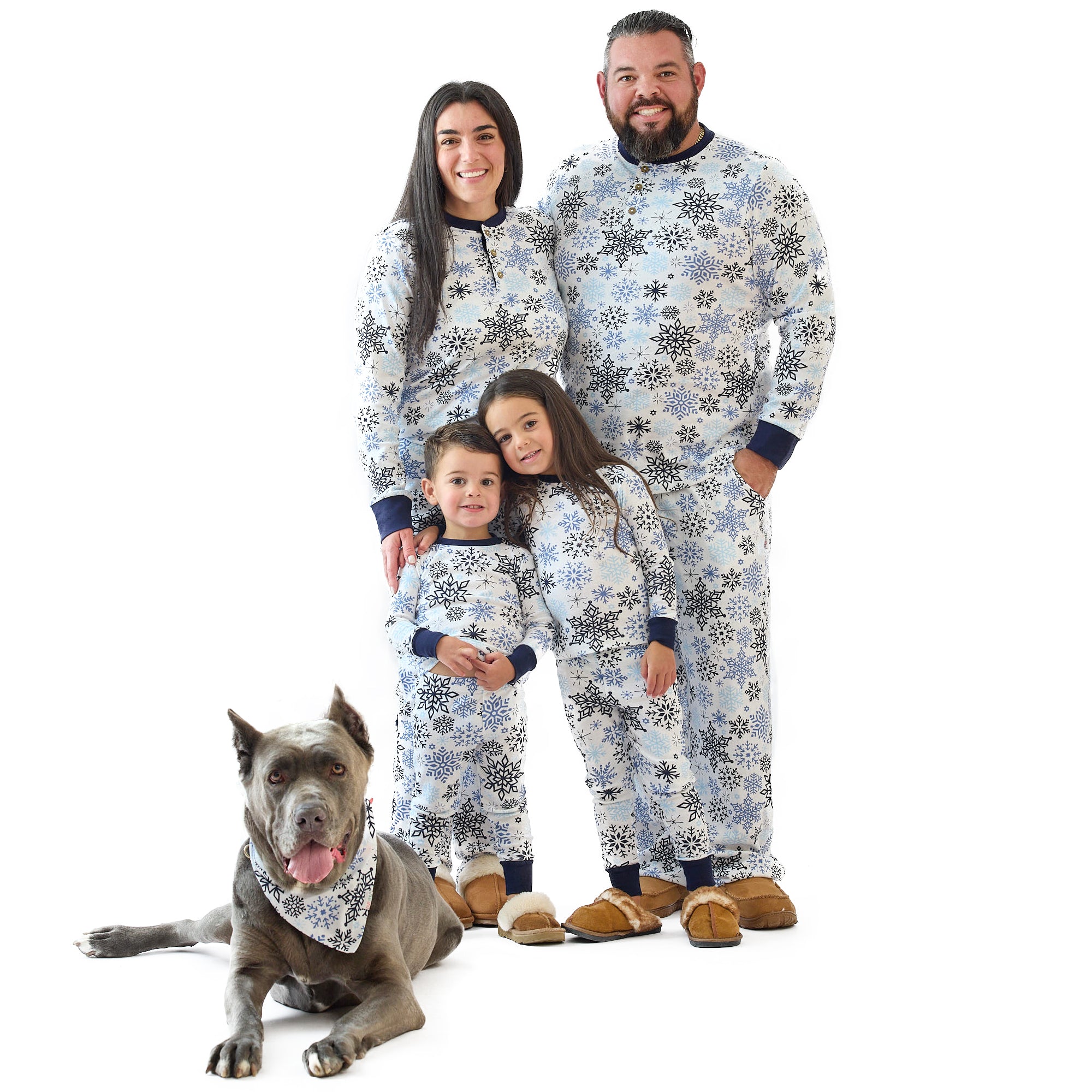 Family of four wearing matching snowflake-patterned pajamas with a dog sitting next to them on a white background.